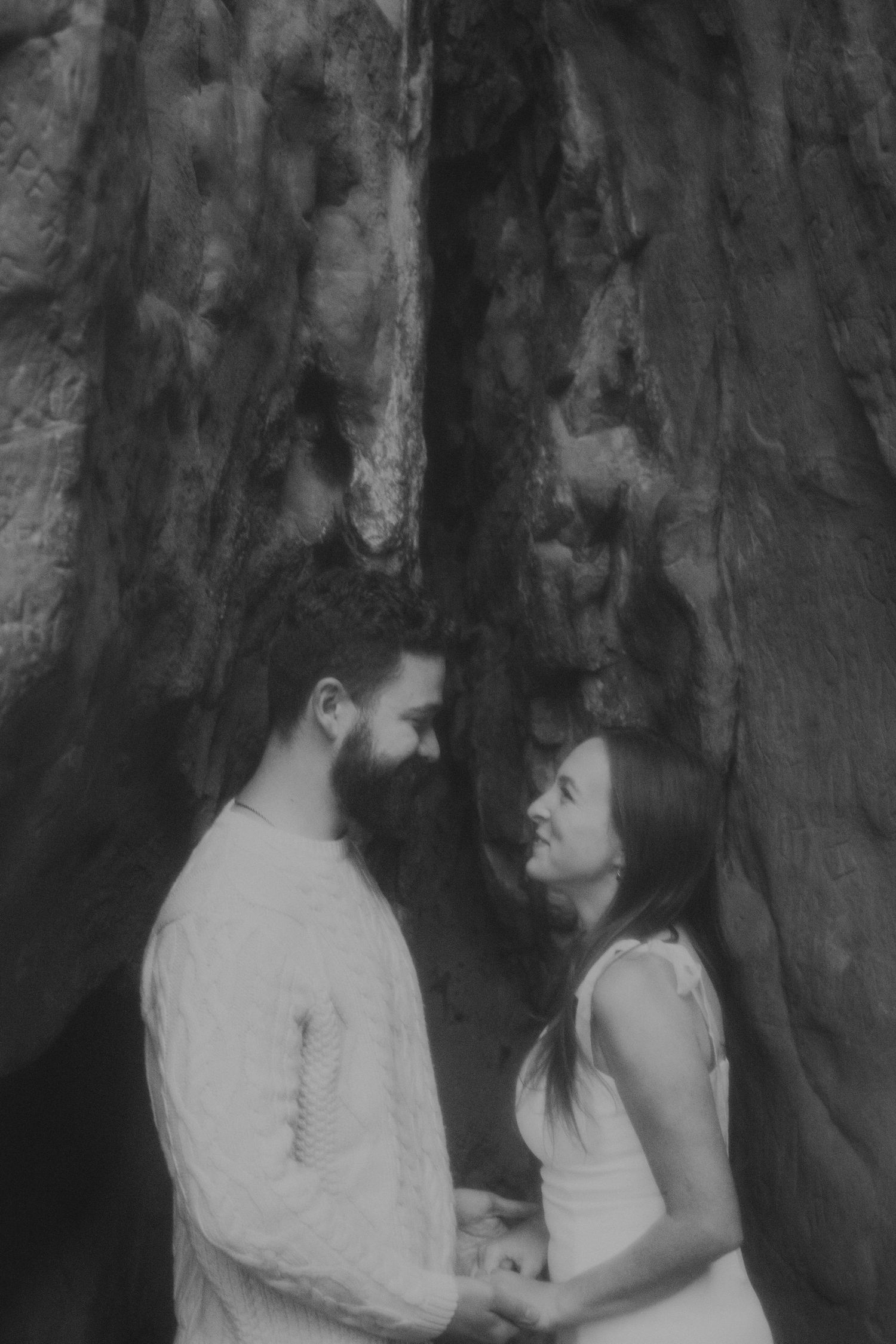 Black and white portrait of couple sharing intimate moment against dramatic rock wall.