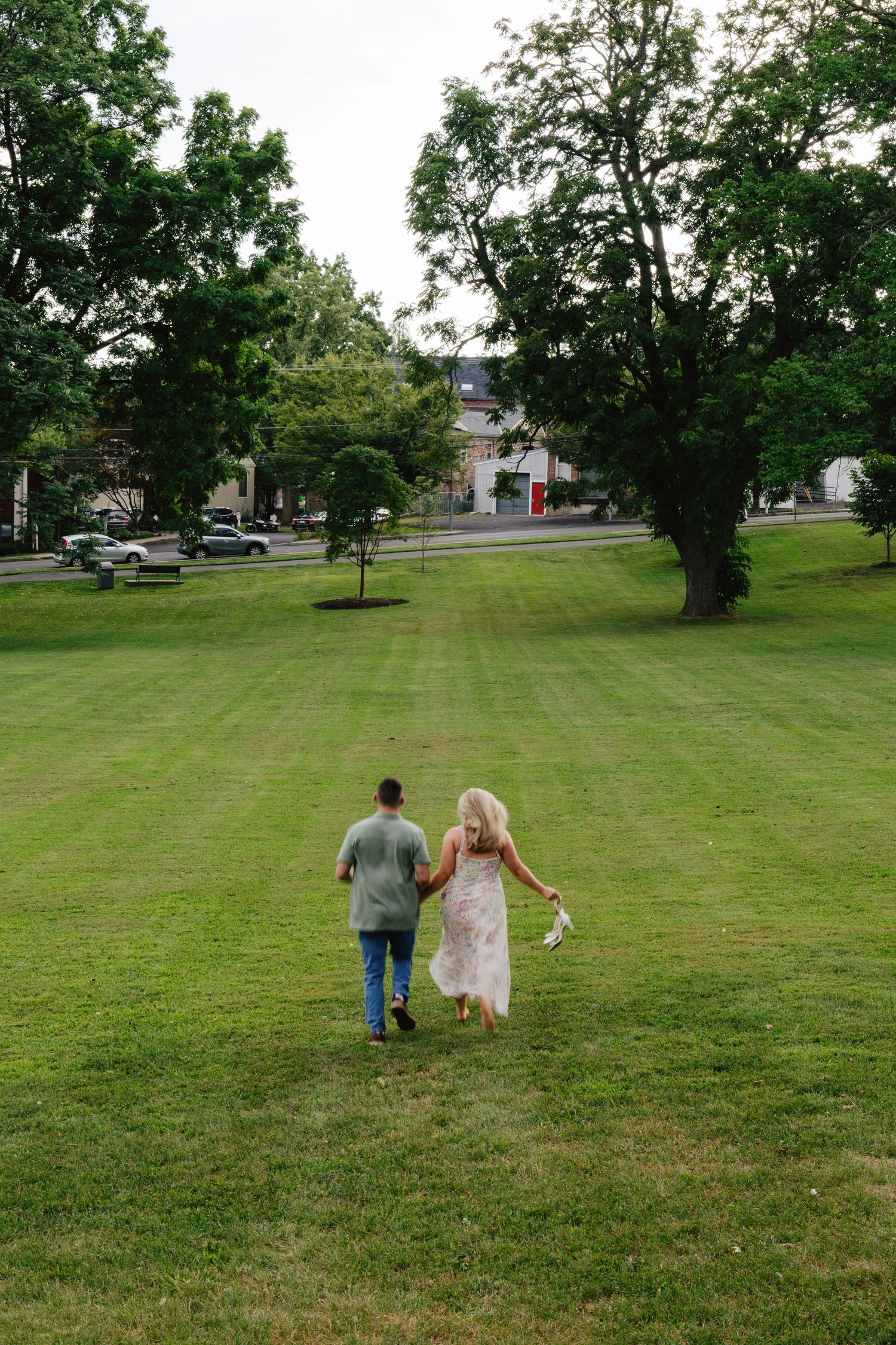 A couple walks hand in hand across a serene green lawn on a summer day.