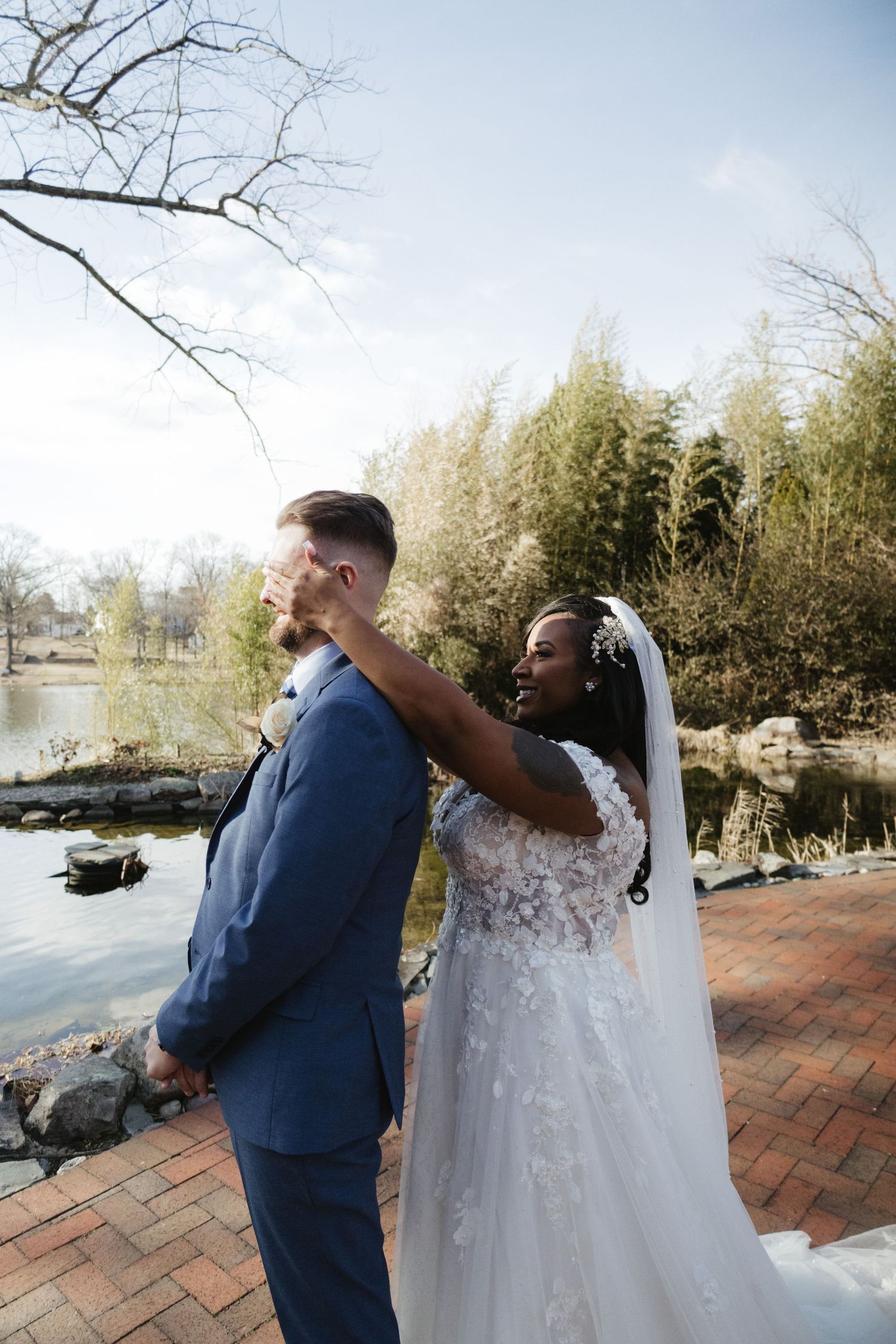 Wedding couple sharing a playful first look moment by a scenic pond.