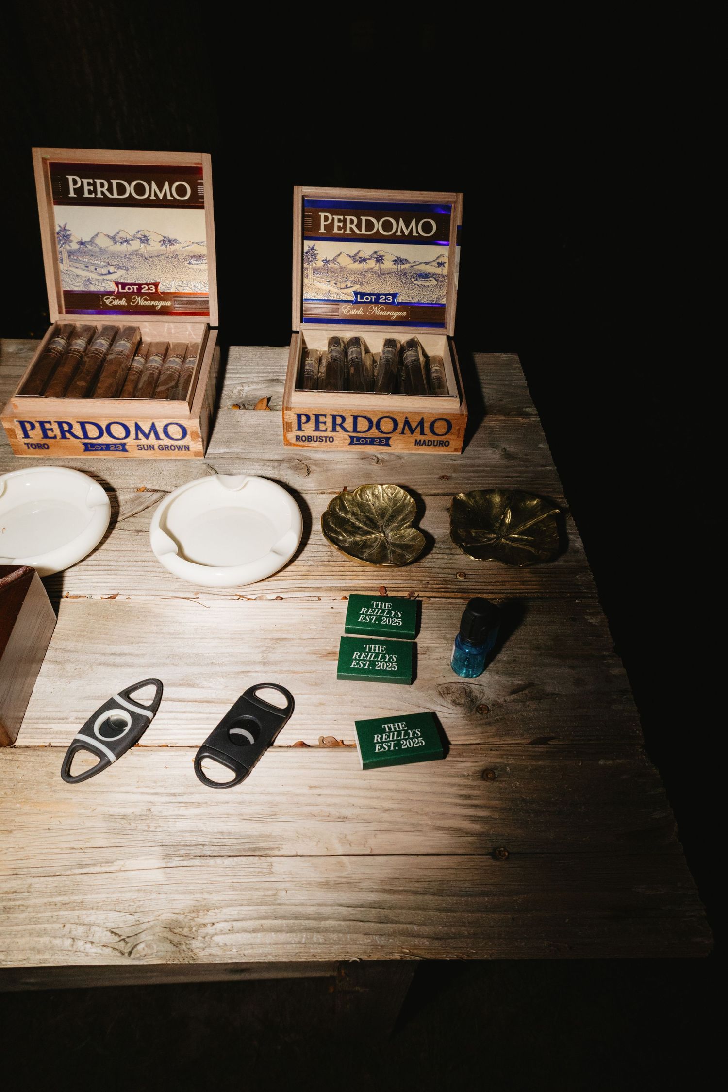 Perdomo cigar boxes and cigar accessories including cutters and lighters displayed on a rustic wooden surface.
