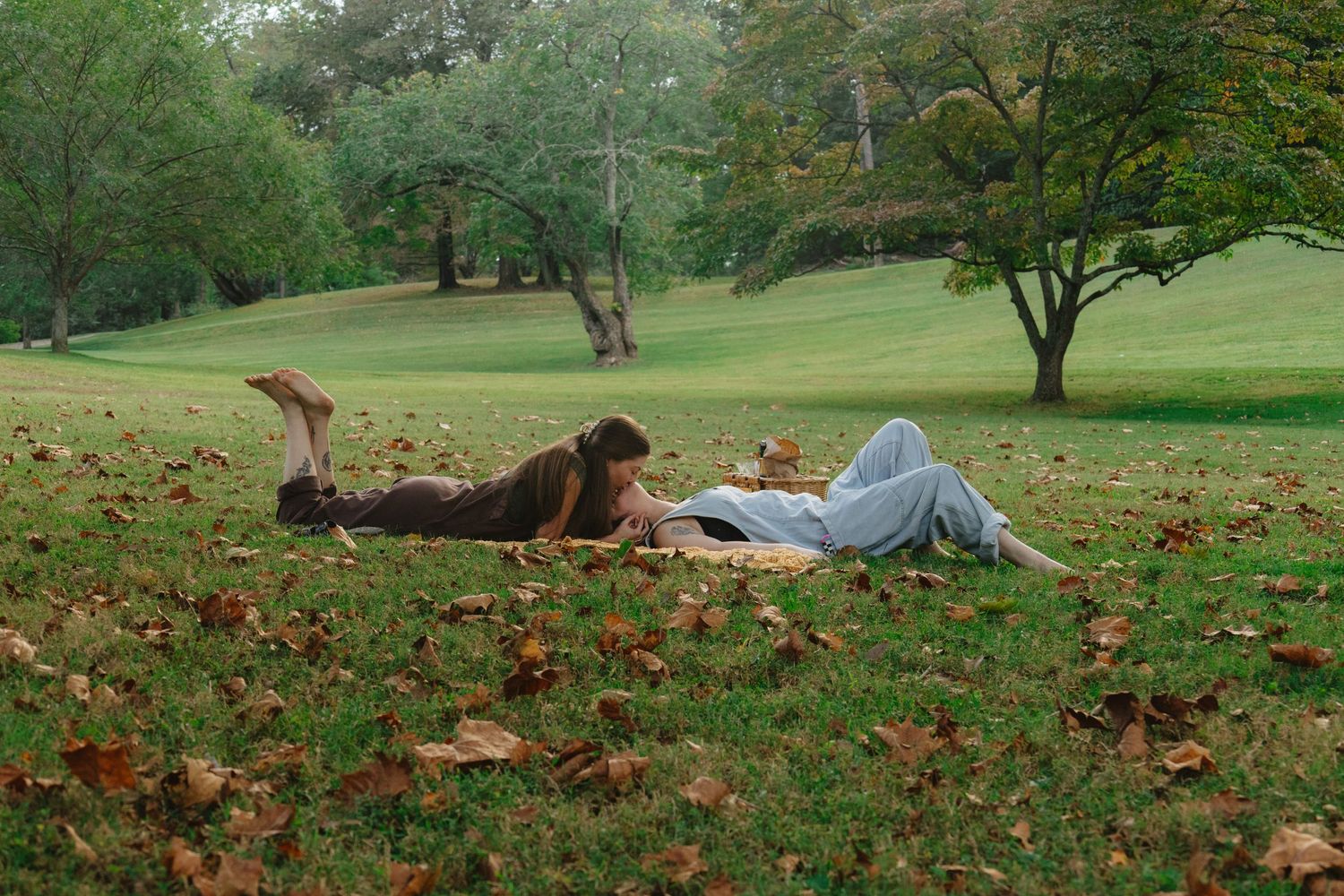 A series of autumn scenes show someone laying in fallen leaves on a grassy hill in a park setting.