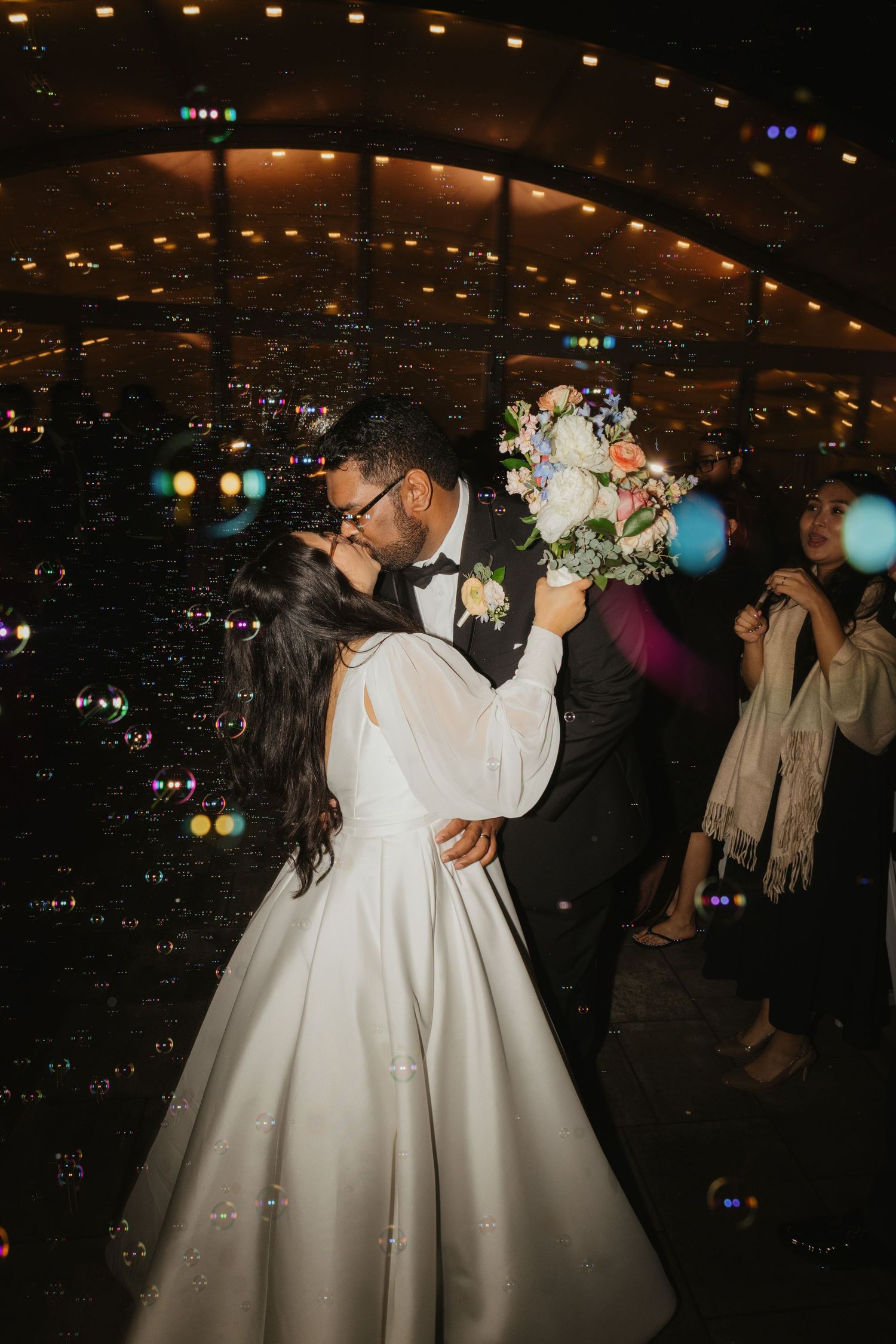 A couple shares a romantic dance moment at a wedding reception with city lights twinkling in the background.