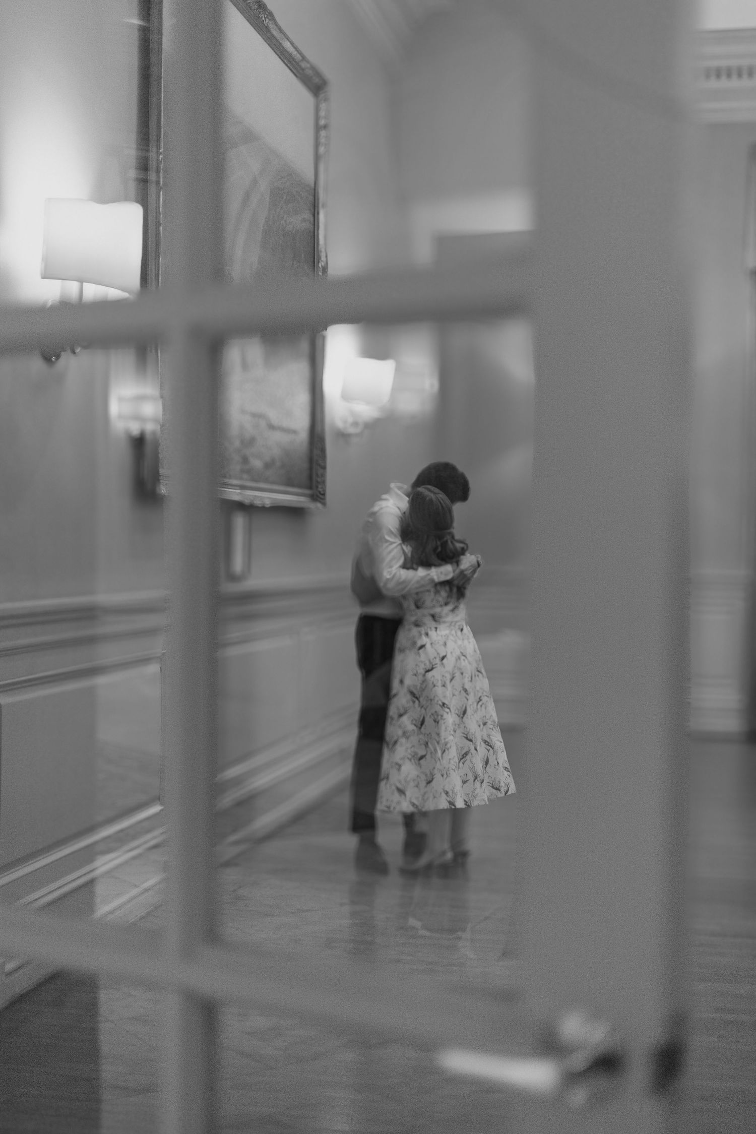 A couple shares an intimate dance moment in an elegant room viewed through a window frame.