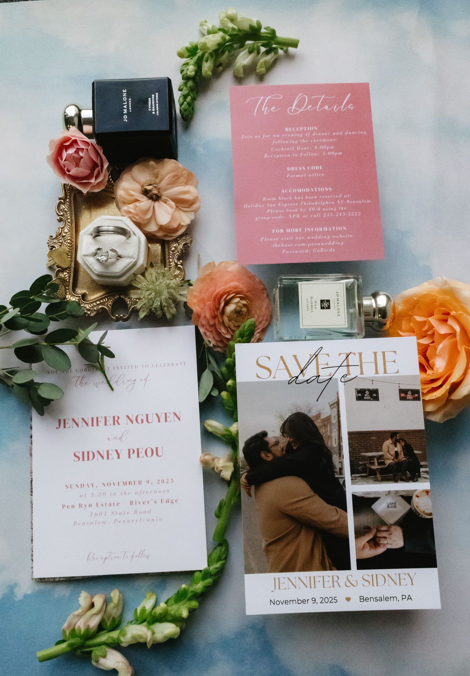 Wedding invitation suite with pink and white stationery, roses, and decorative elements laid out on a blue-grey surface.
