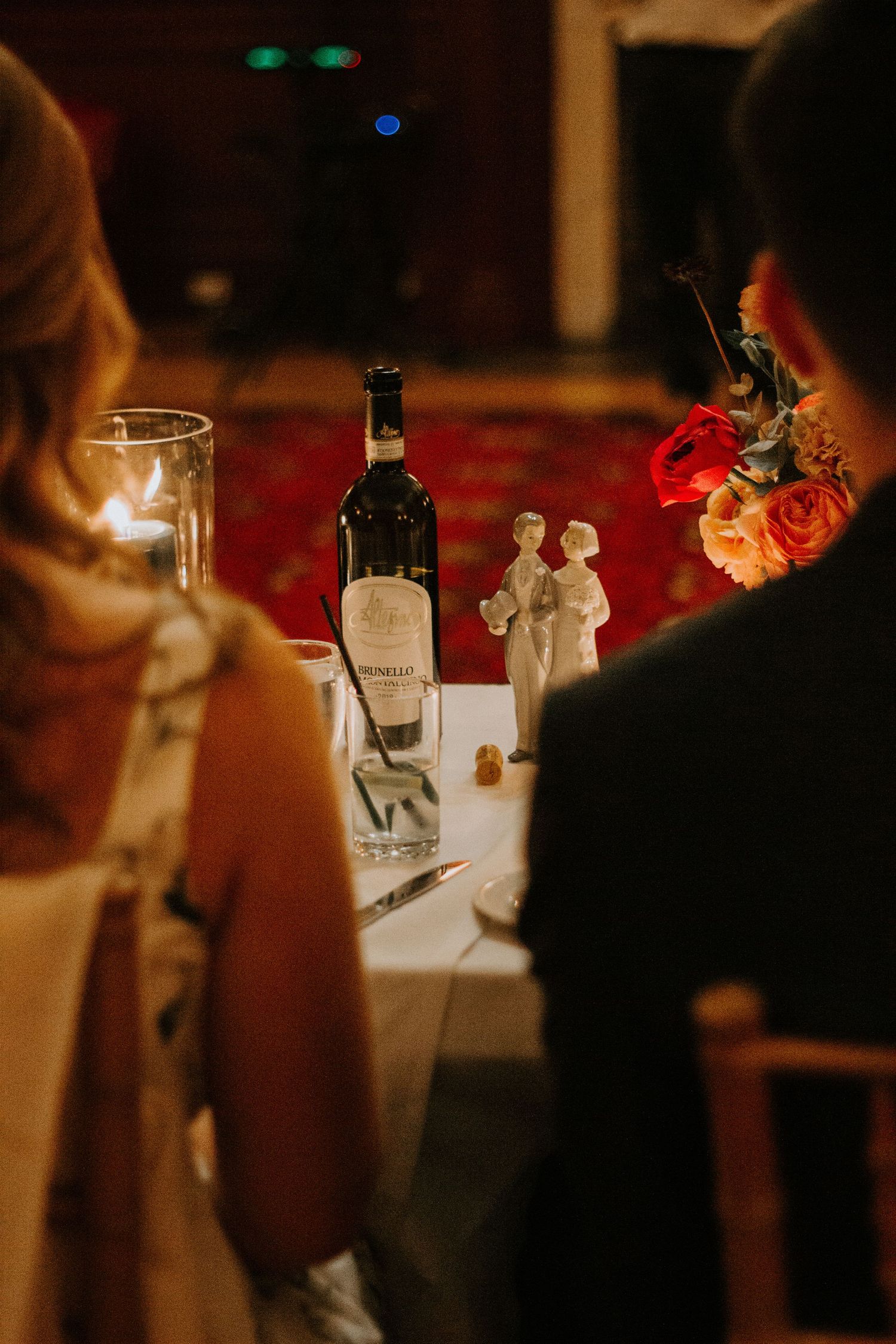 A wedding table setting with wine bottle and small cake topper figurines.