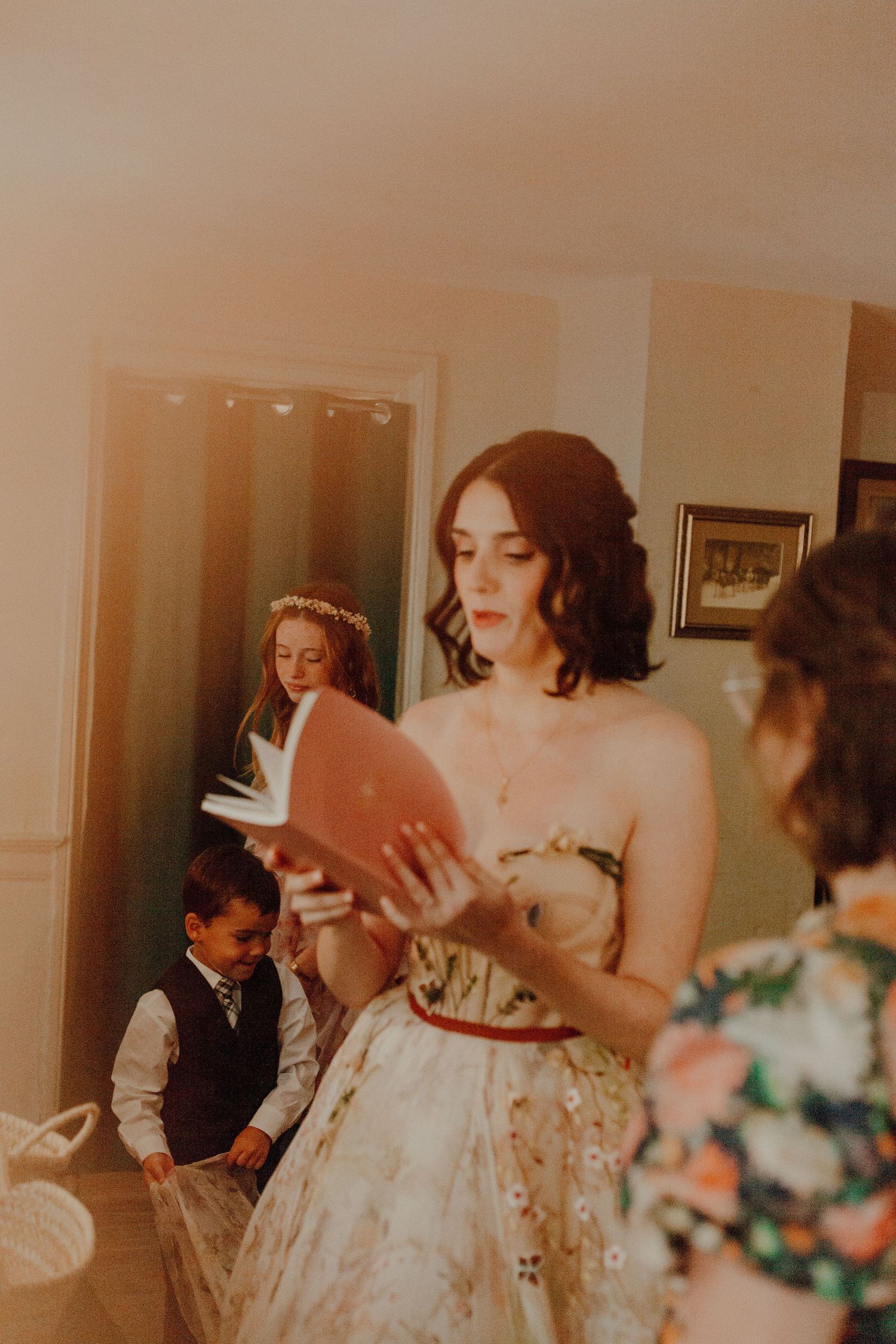 A person in a floral dress reads from a book during a wedding preparation.