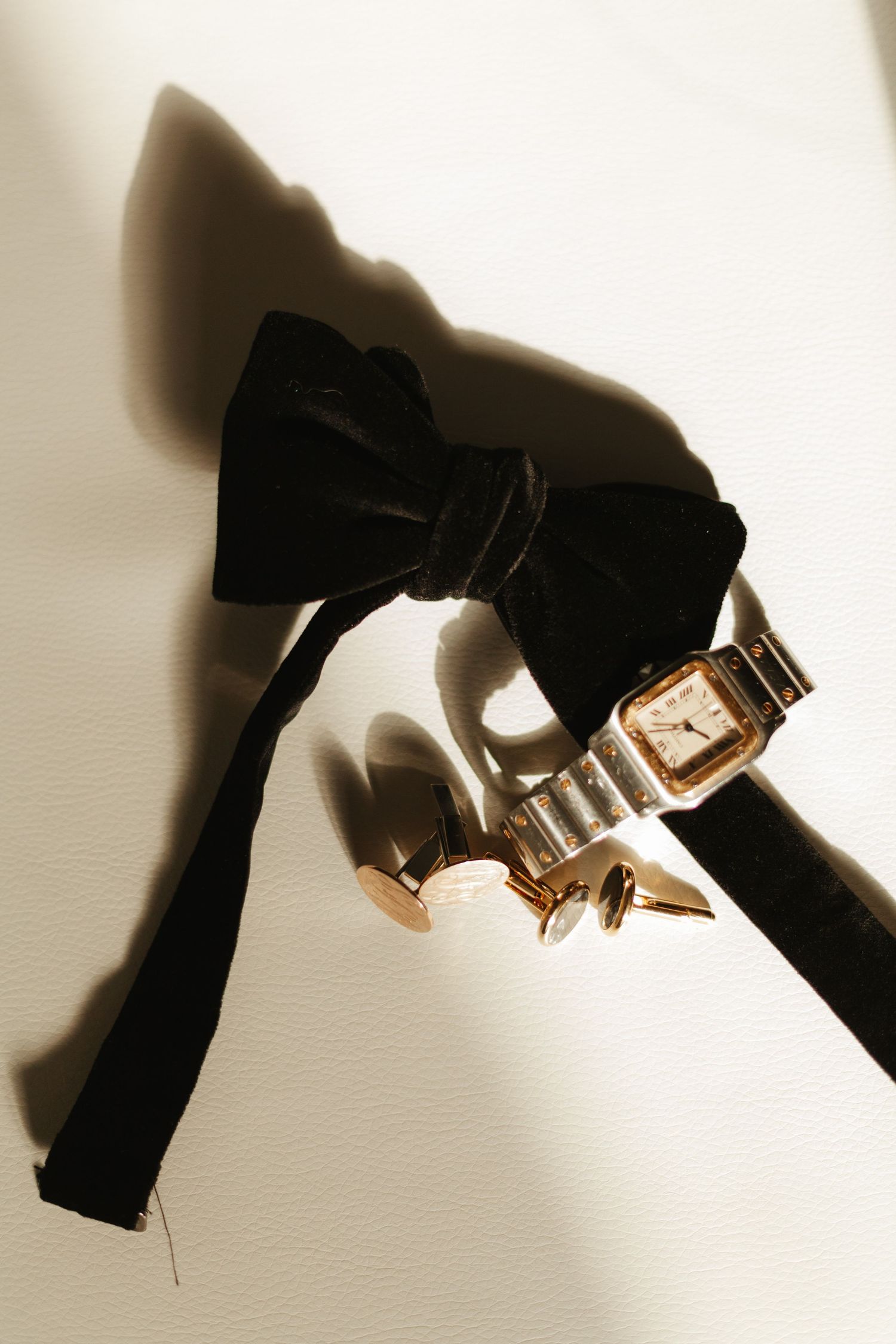 Stylish black bow tie and gold watch arranged artistically with dramatic shadow.