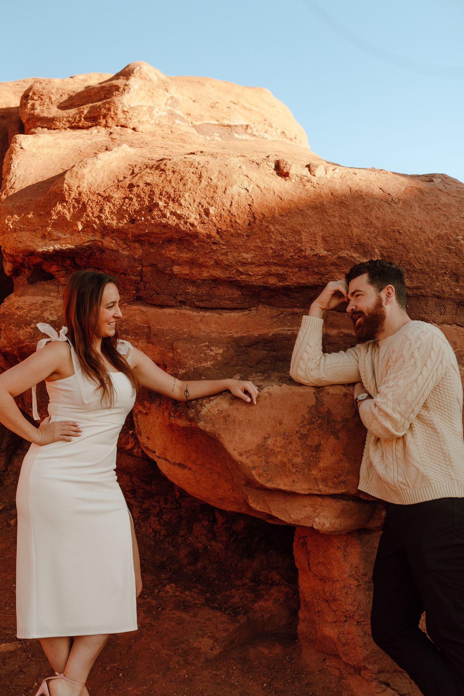 A couple poses playfully against red rock formations in a desert landscape.