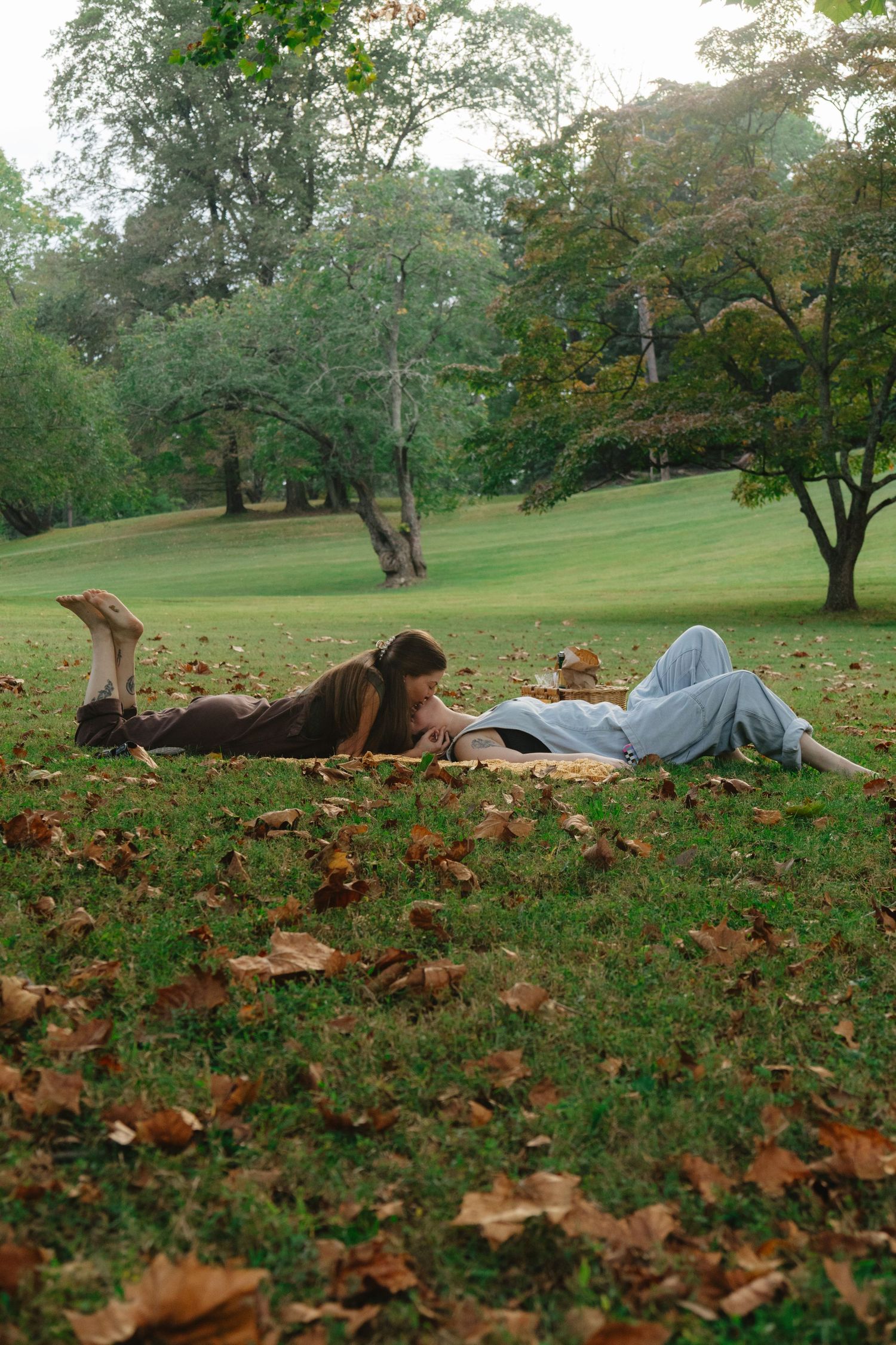 A sequence of photos showing someone lying in autumn leaves on a grassy hill surrounded by trees in a park setting.