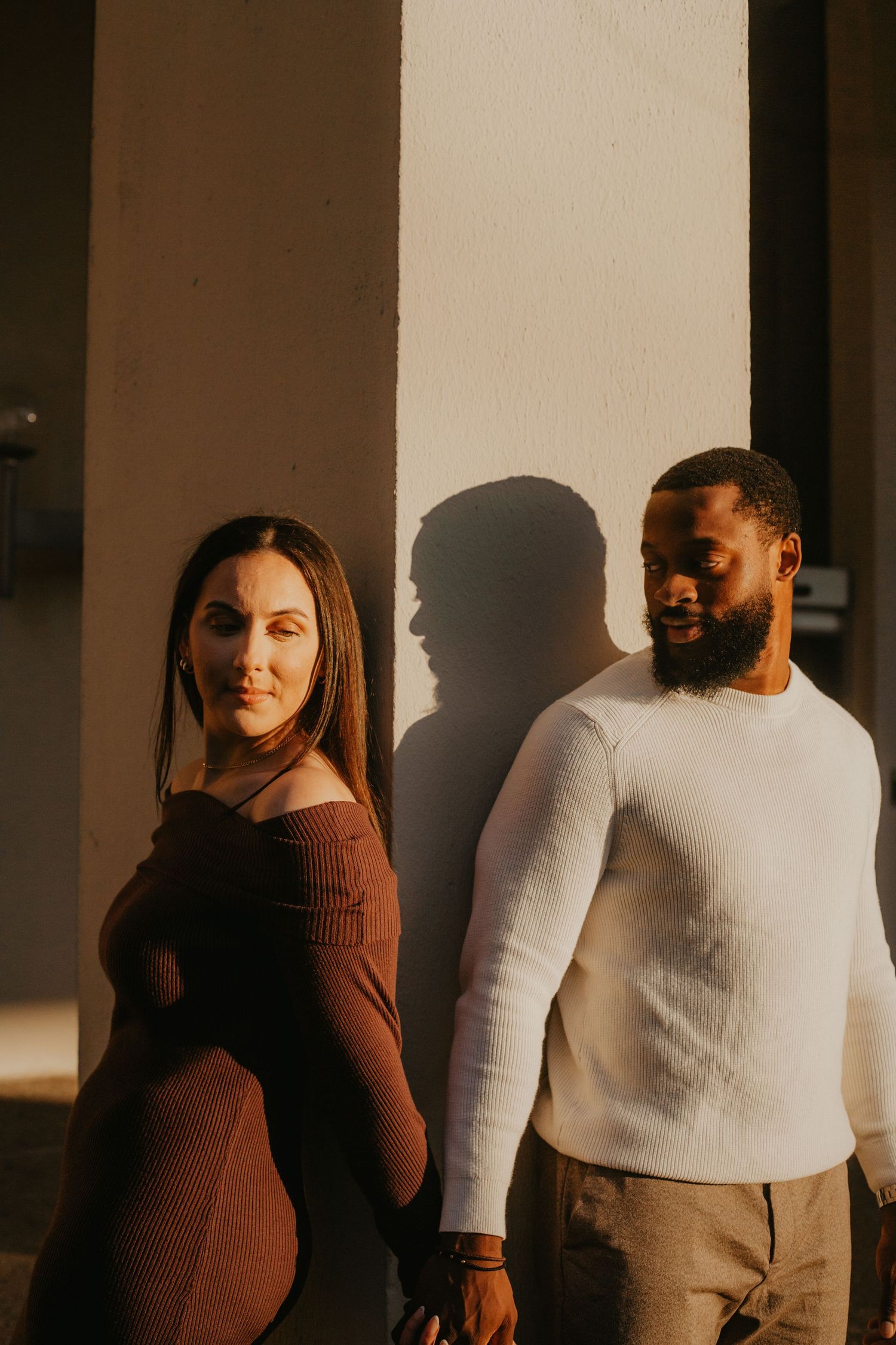 A couple in casual sweaters poses together in golden sunlight casting dramatic shadows.