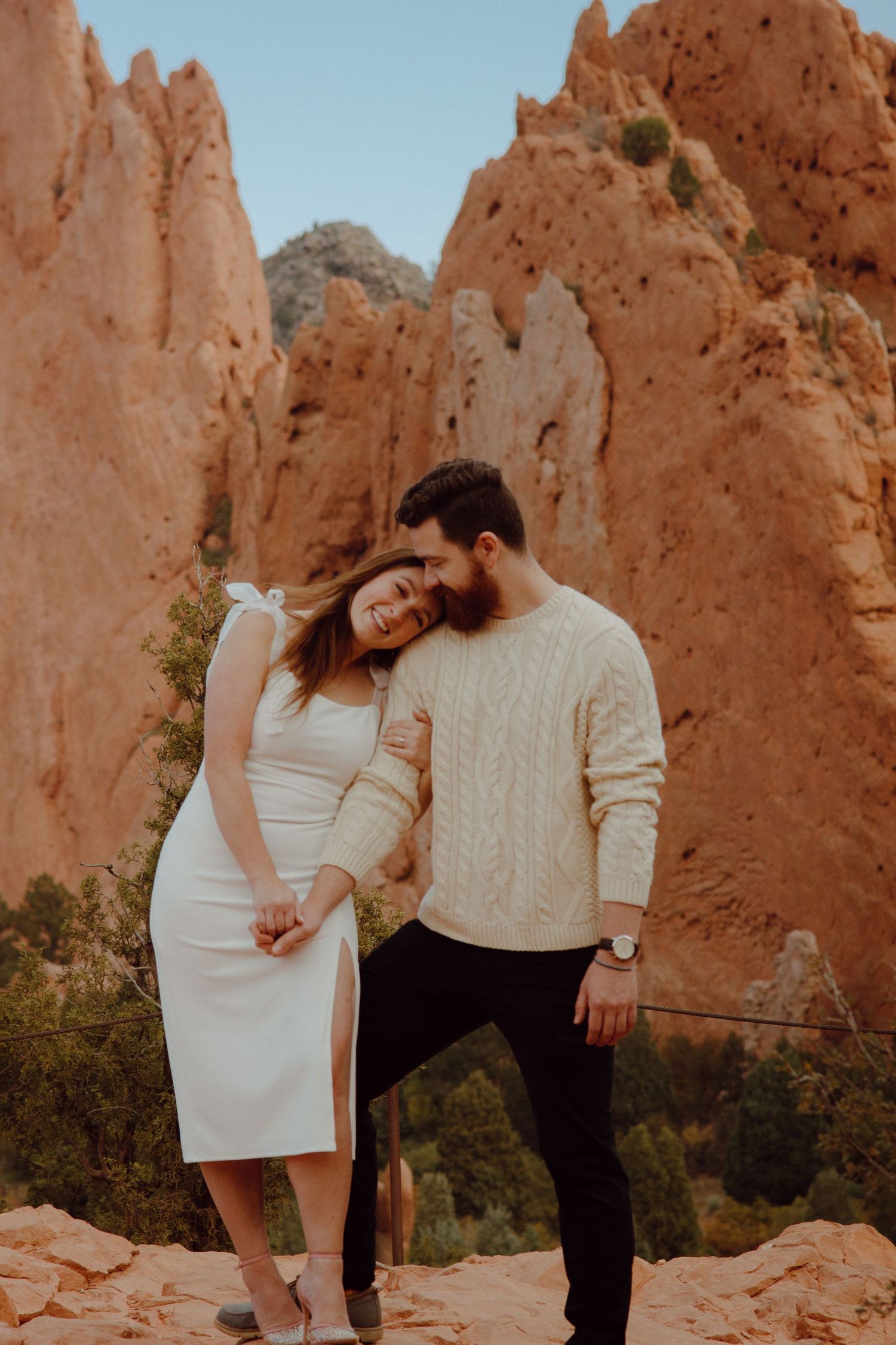 A couple shares a romantic moment amid towering red rock formations at sunset.