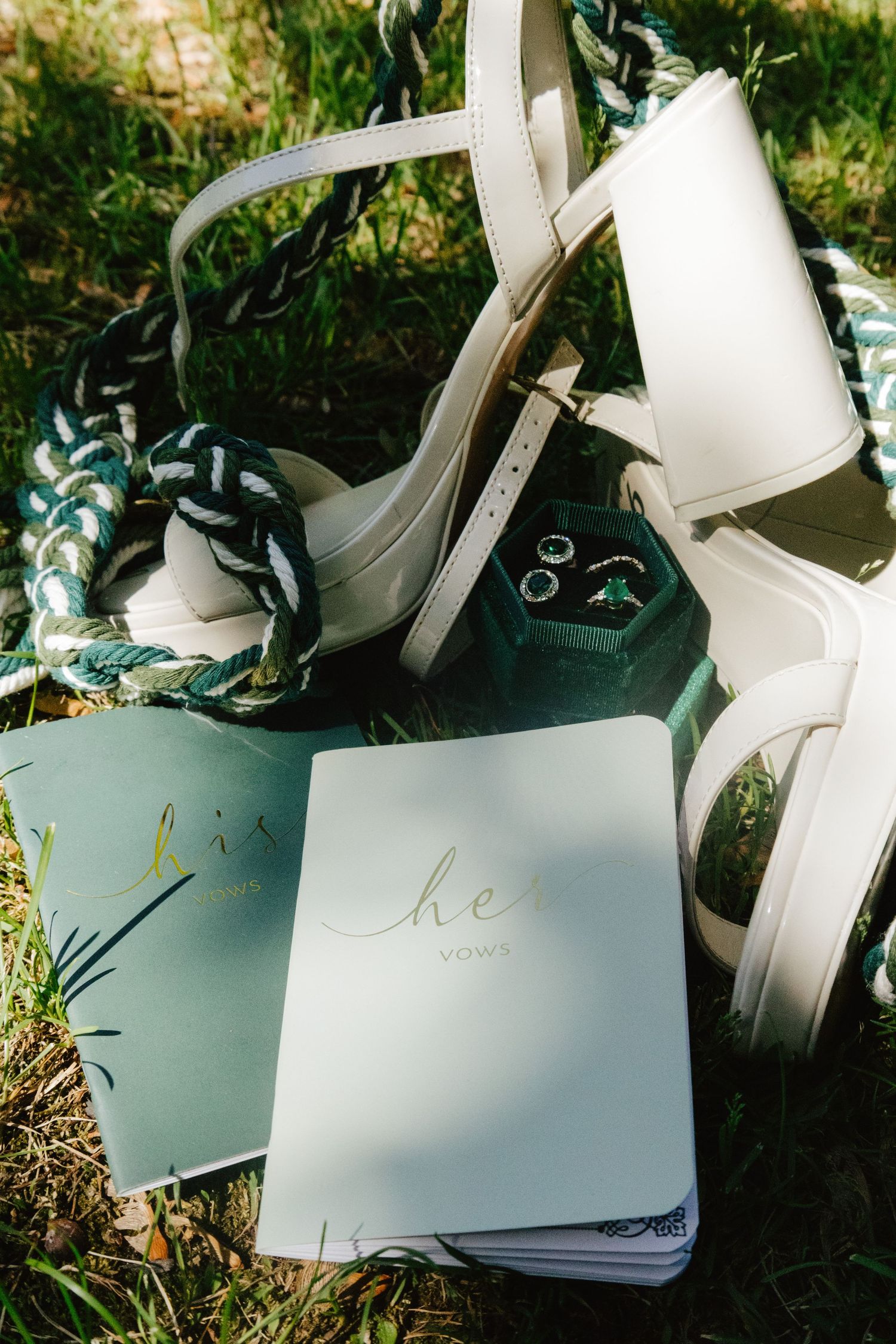 Wedding vow books and accessories arranged on grass in soft natural light.
