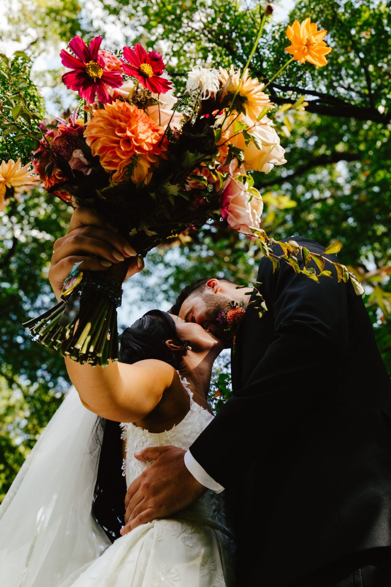 A romantic wedding moment captured outdoors with vibrant autumn flowers and natural greenery in the background.