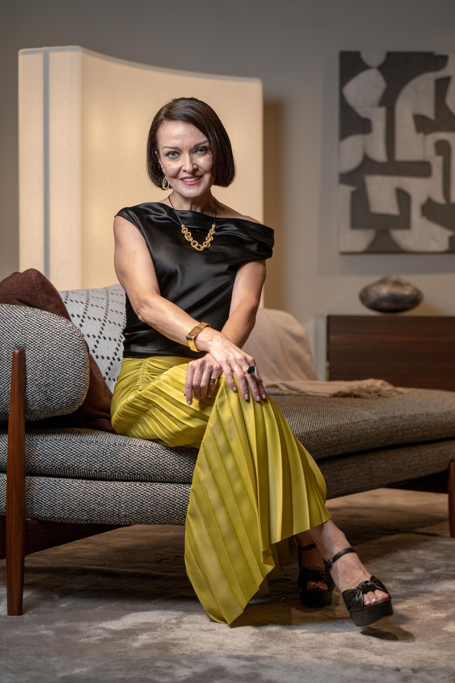 Lifestyle photo of yellow pleated skirt and black top on grey couch.