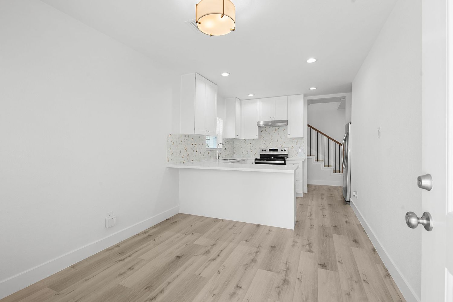 Contemporary open concept living space with light wood floors and white walls illuminated by recessed lighting.