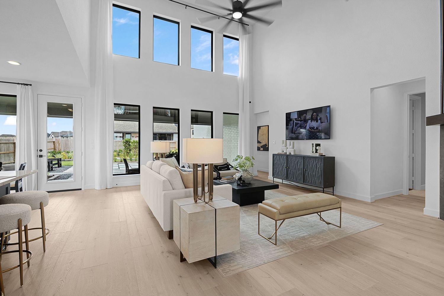 Modern open concept living room with light hardwood floors, white walls, and large windows letting in natural light.