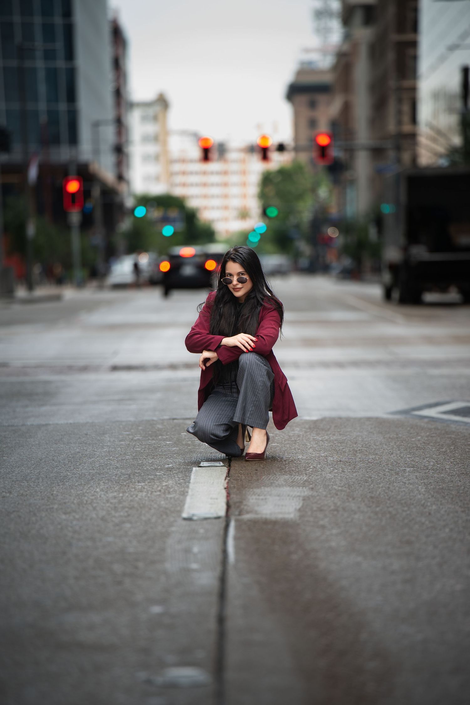 Street fashion photo of someone crouching on a wet city street with traffic lights in the background.