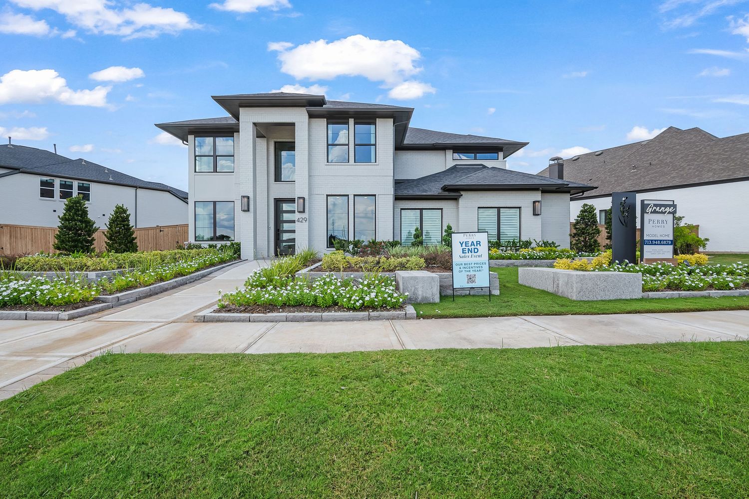 Modern luxury home with white exterior, large windows, and manicured front lawn with colorful flower beds.