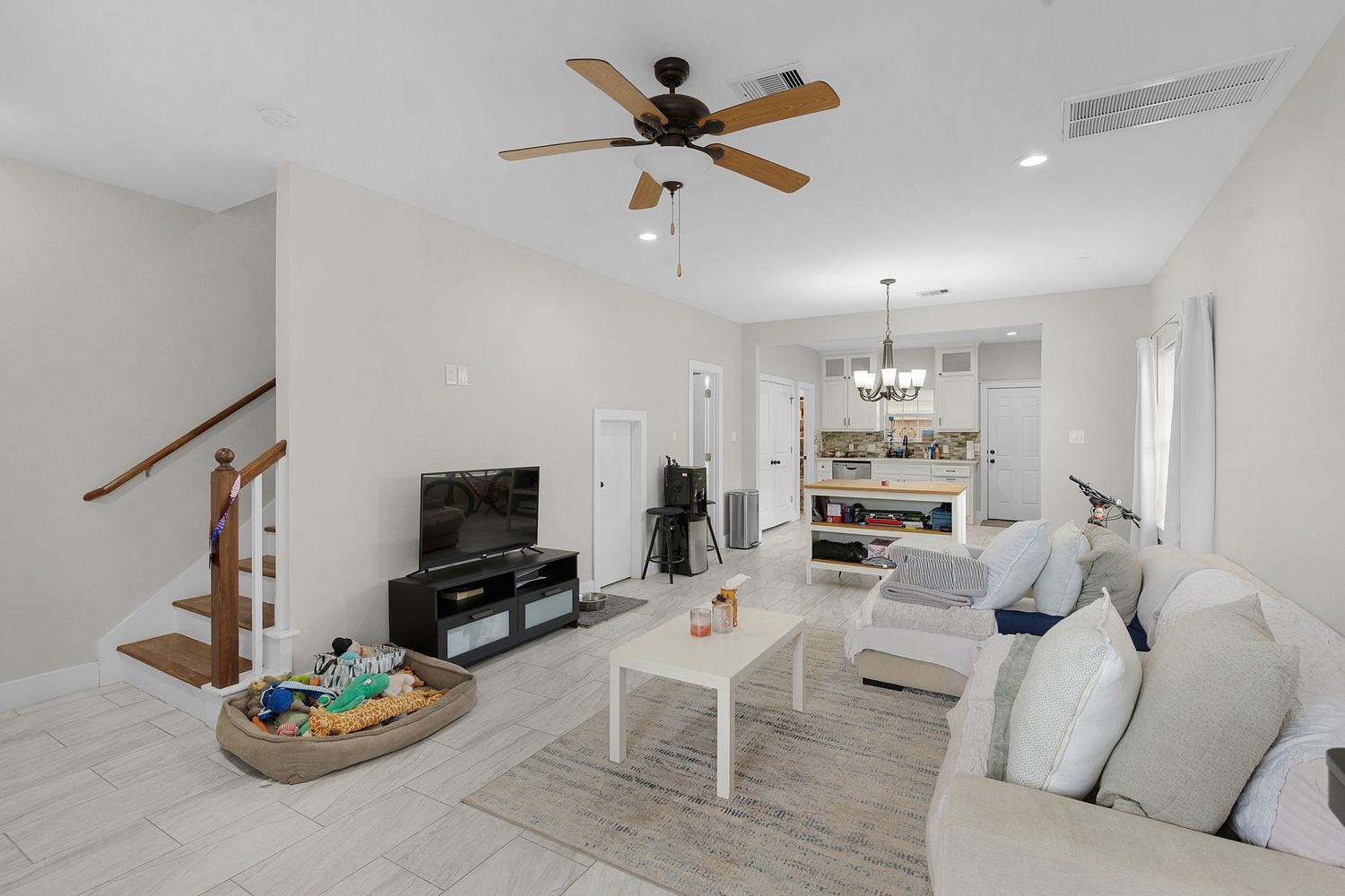Modern white living room and kitchen with wood accents features vaulted ceilings, ceiling fan, and open floor plan design.