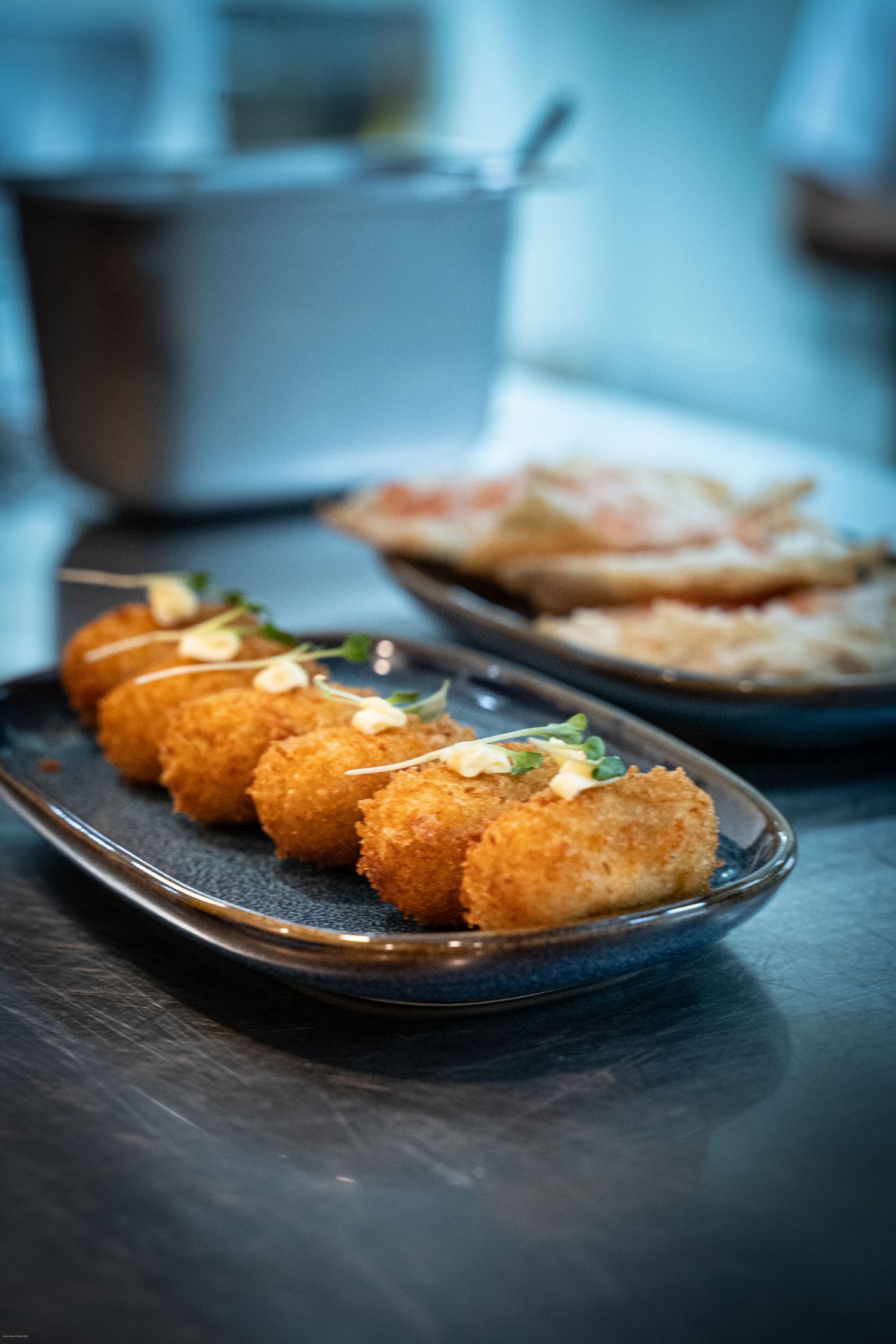 Row of golden fried croquettes garnished with herbs on a dark blue plate.