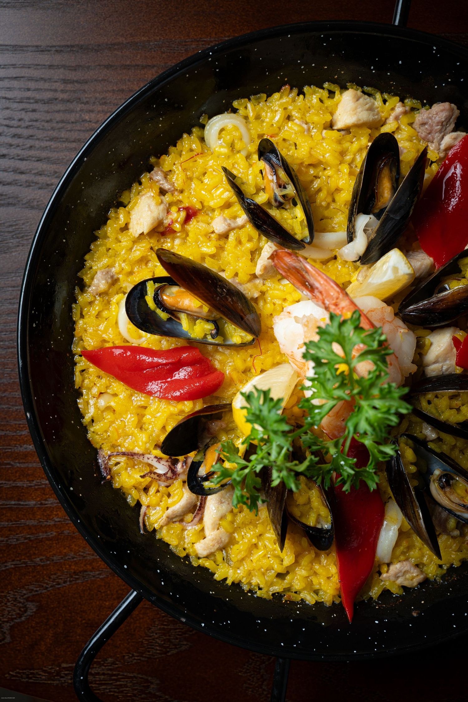 Vibrant yellow paella dish with seafood, mussels, shrimp and red peppers served in a traditional black pan.