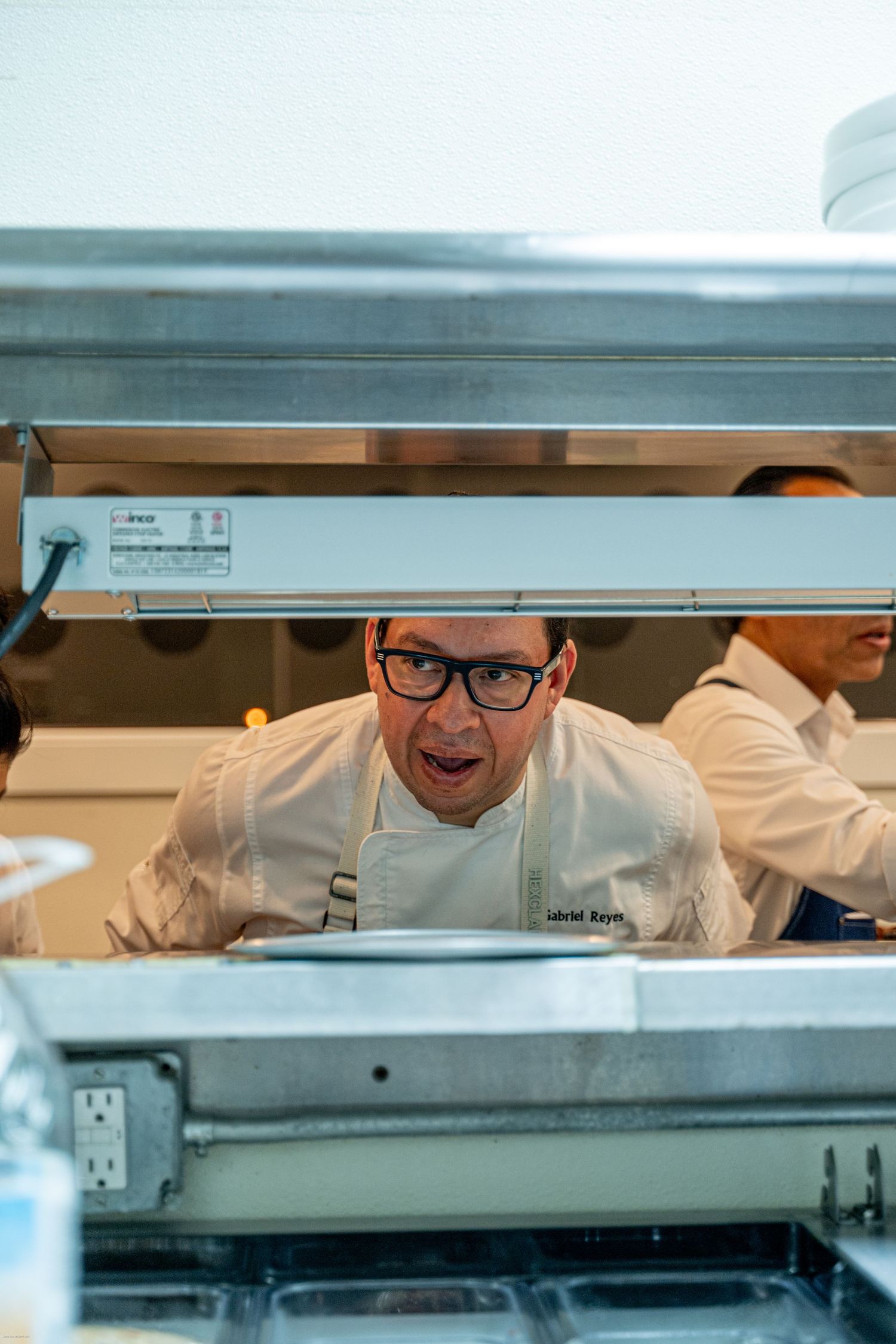 Restaurant kitchen pass-through window with chefs peeking through during service.