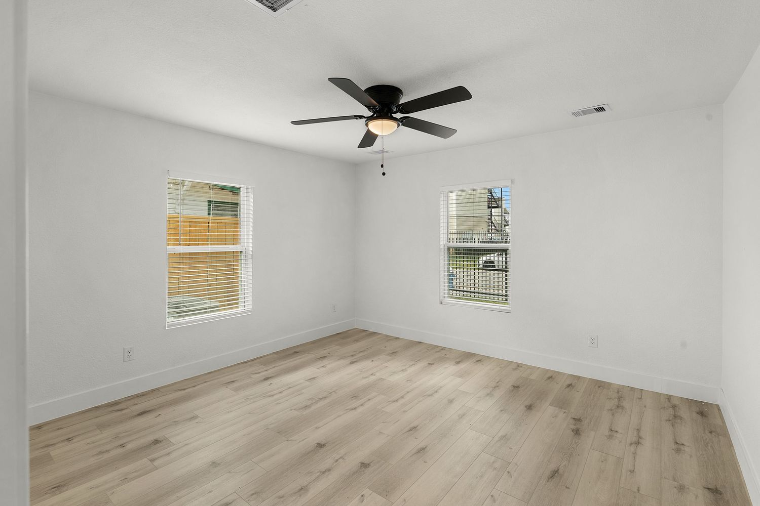 Empty living room with light wood floors, white walls, and ceiling fan in new construction home.