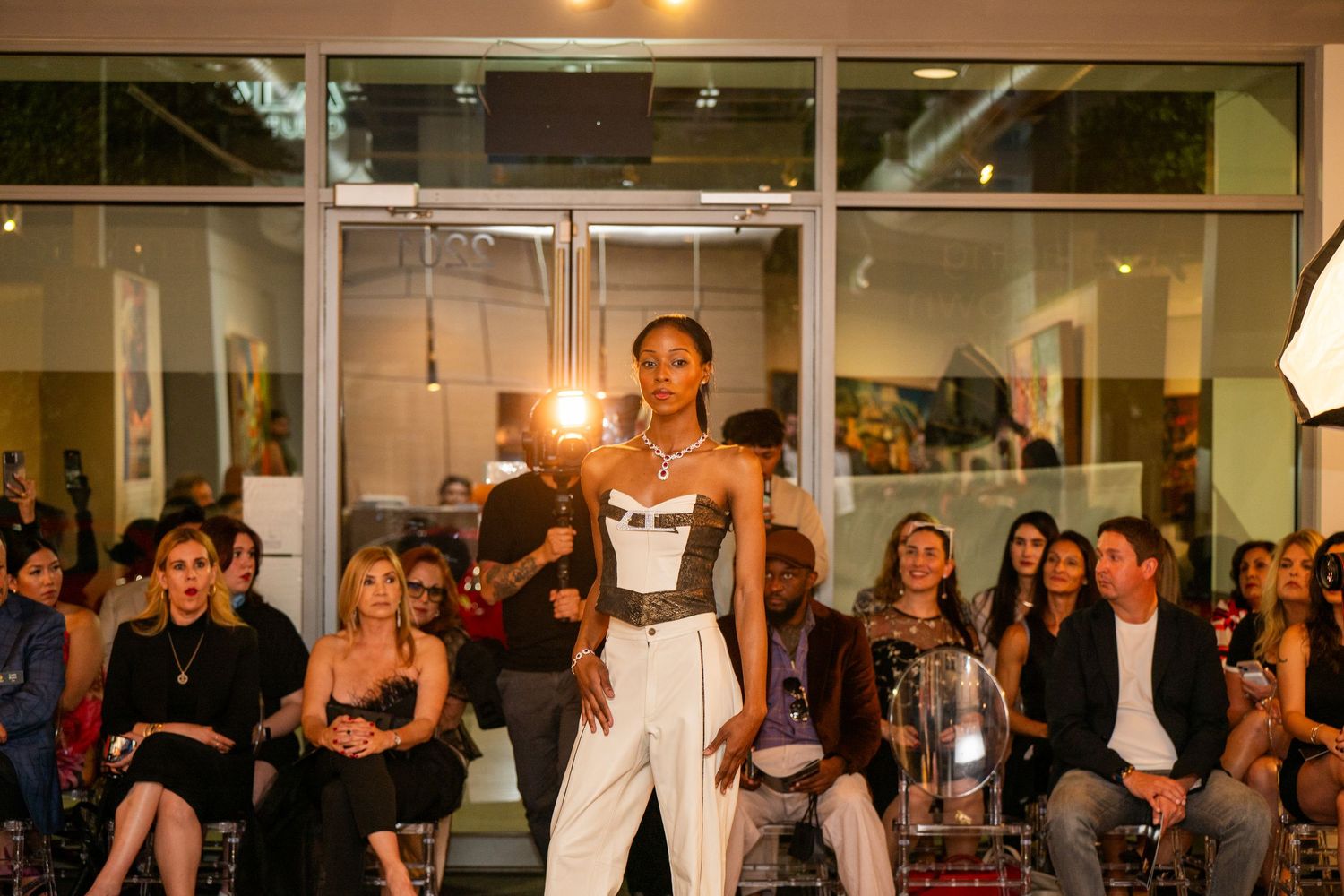 Fashion model walking at a live event in Houston, Texas, with audience visible in the background. Captured in action with event lighting, i