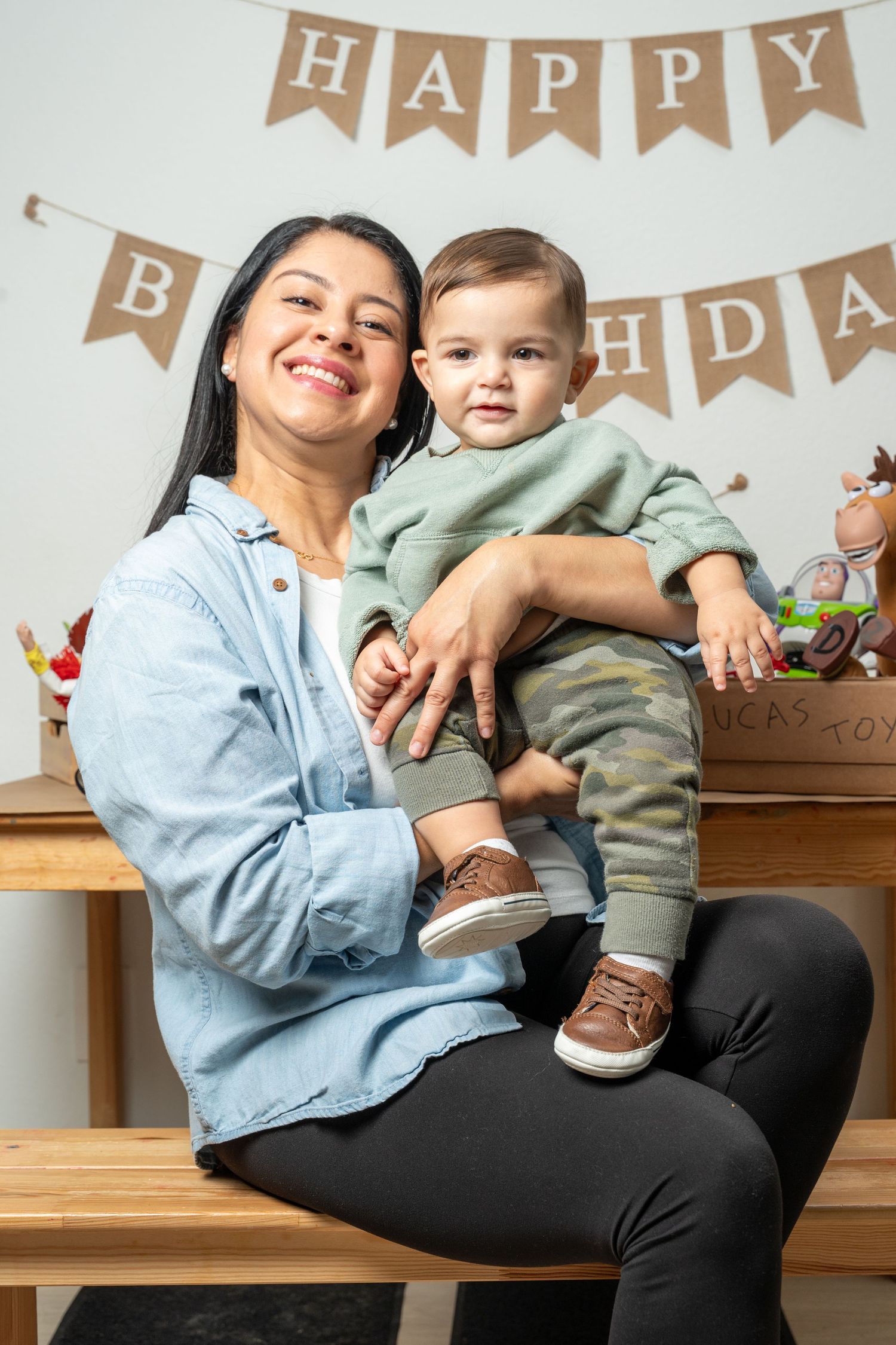 A parent and child share a tender moment on a wooden bench under a 'Happy Birthday' banner decoration.