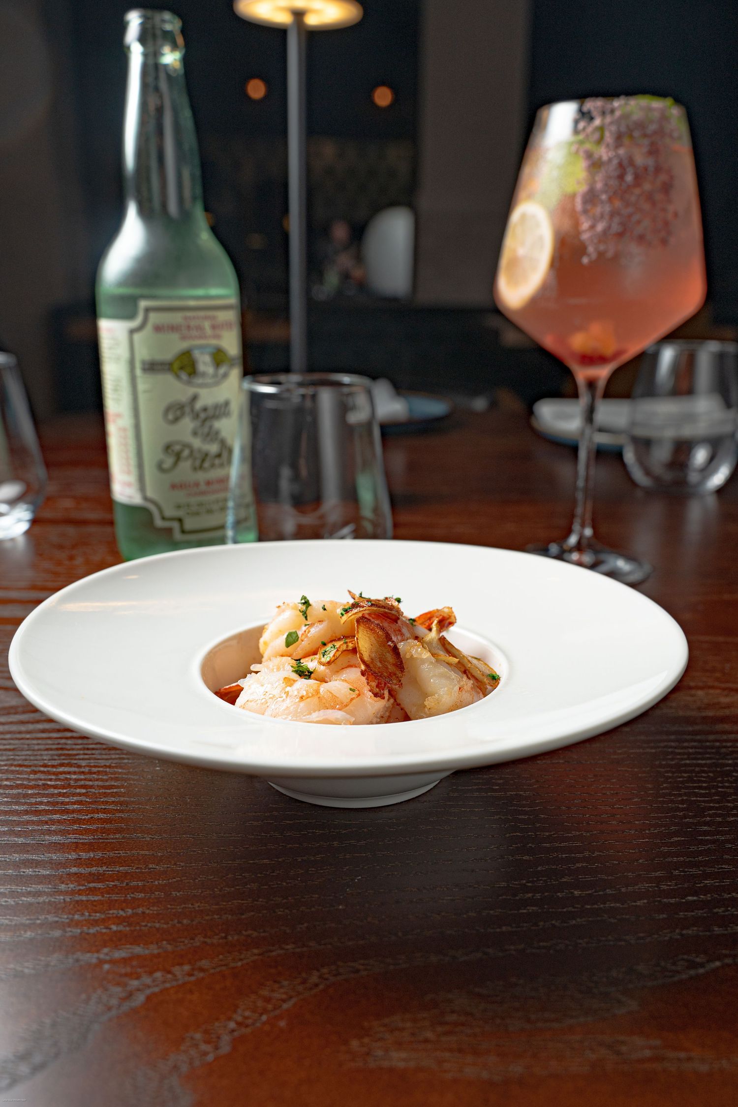 Fine dining plate presentation on dark wooden table with beverage glasses in background.