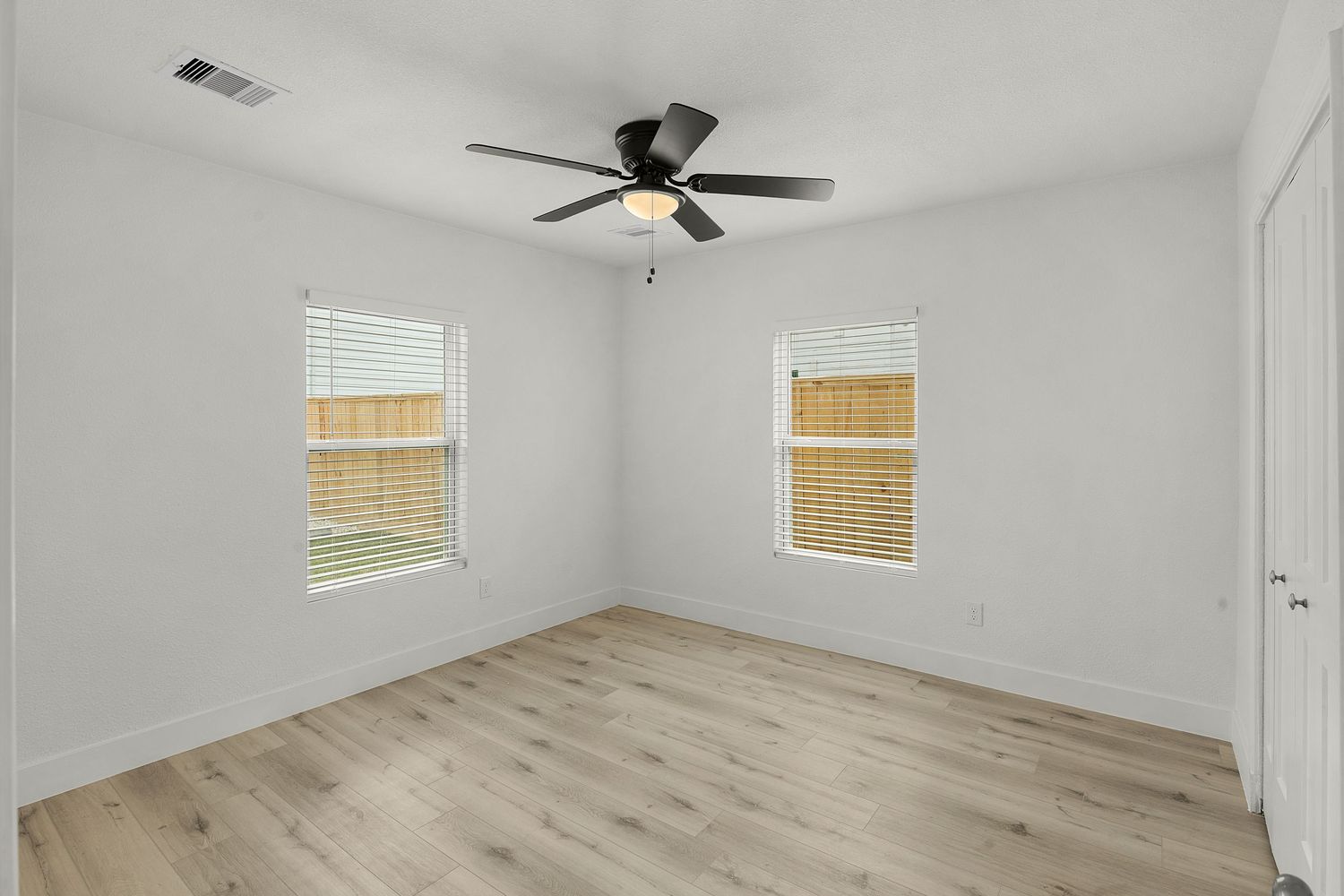 Spacious unfurnished room with two windows, light wood floors, and white walls perfect for a bedroom setup.
