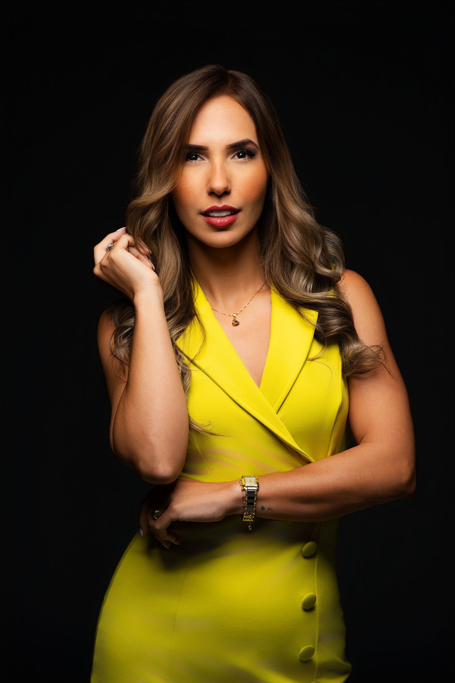 Professional portrait of a model in a sleek yellow sleeveless dress against a dark background.