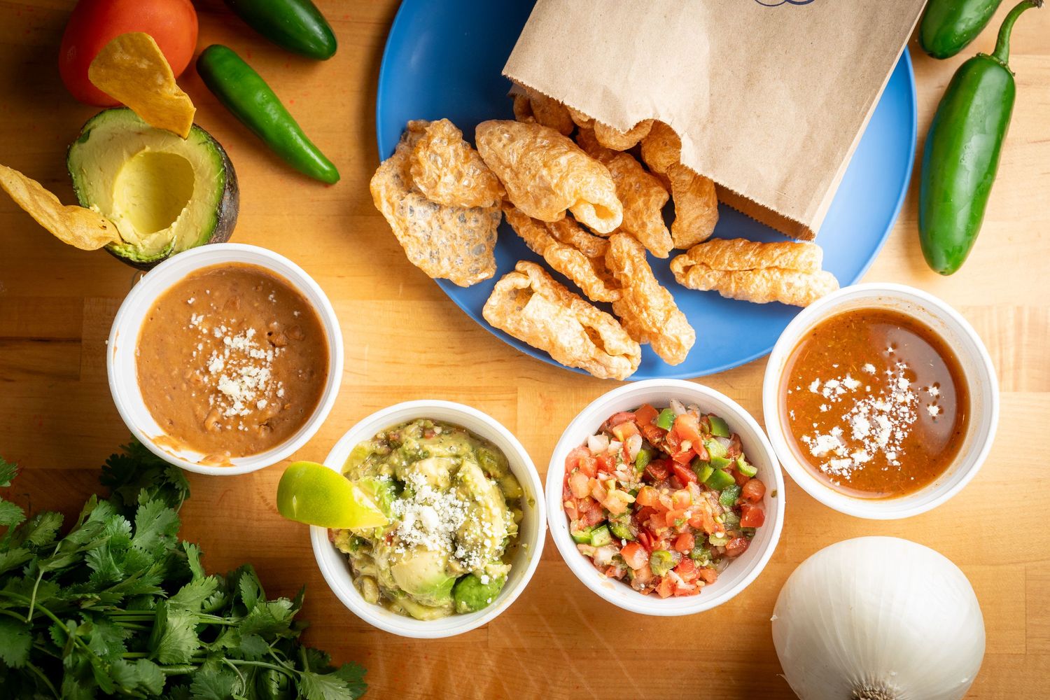 Fresh jalapeño peppers, spicy meat, dipping bowls, and various Mexican sauces on a wooden table setting.