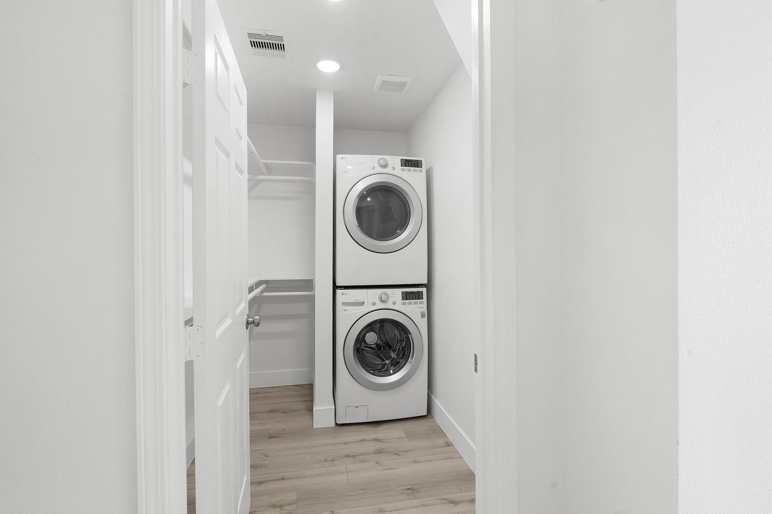 Modern laundry room with stacked washer and dryer units in a bright white hallway with light wood flooring.