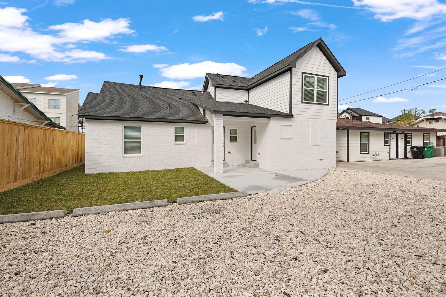 Row of newly built suburban homes with gravel driveways under a bright blue sky with white clouds.