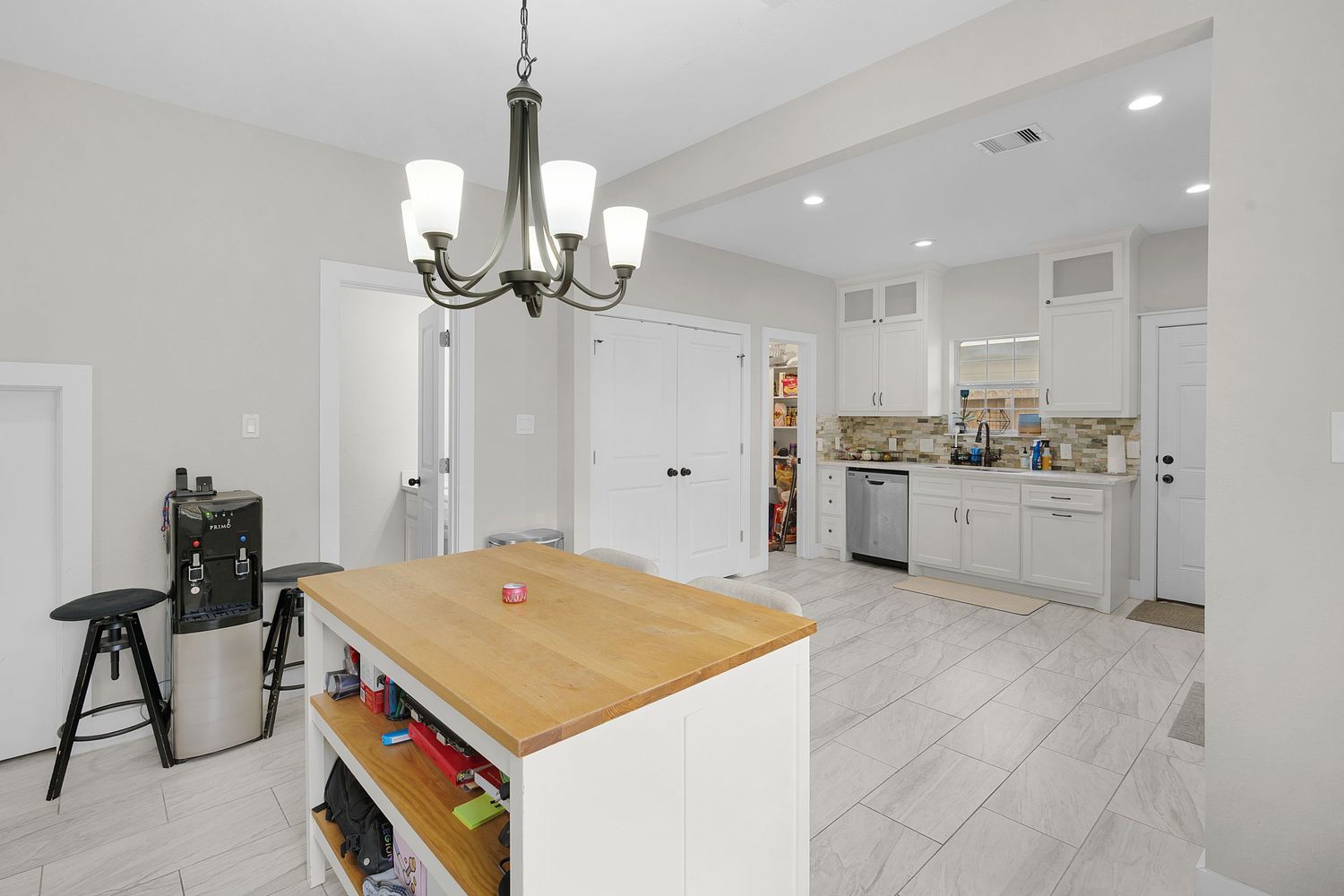 Dining area with wooden table and chandelier adjacent to white kitchen cabinets.