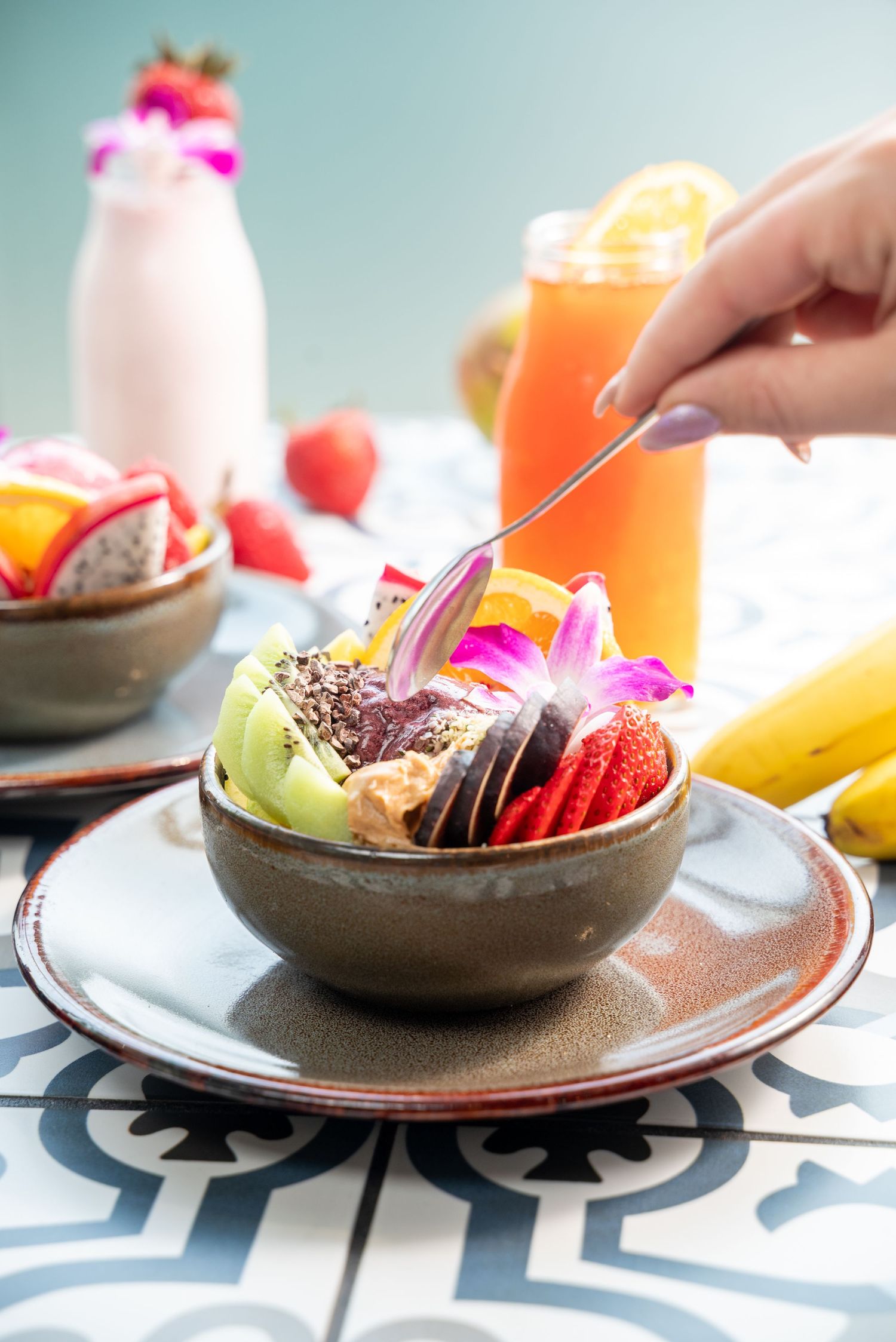 Acai bowl with fresh fruits and edible flowers served with orange juice and pink smoothie.