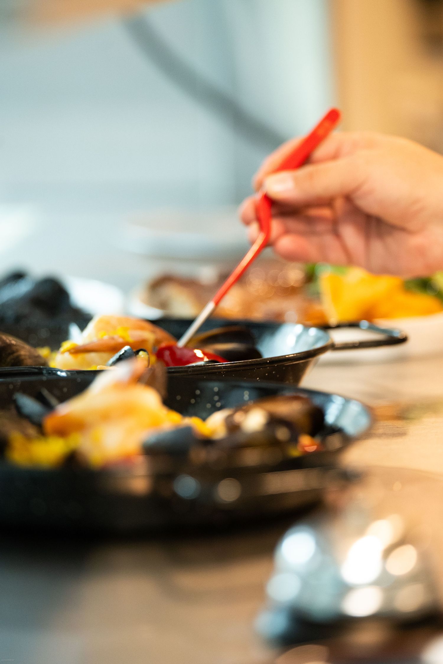 Close-up sequence of hands using red utensils to plate food on dark dishes.