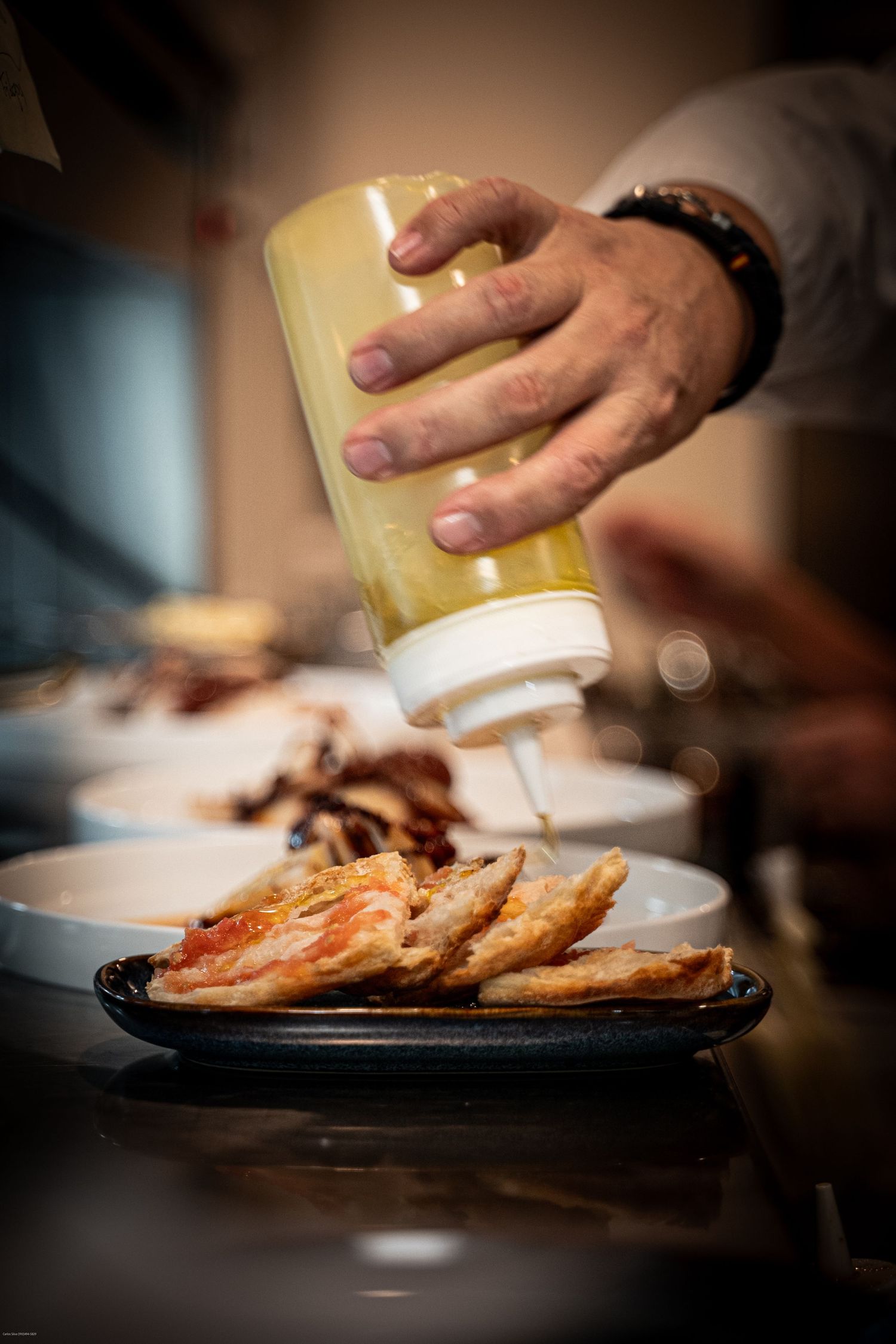 Hands preparing a gourmet dish with bacon strips being plated on a dark surface.