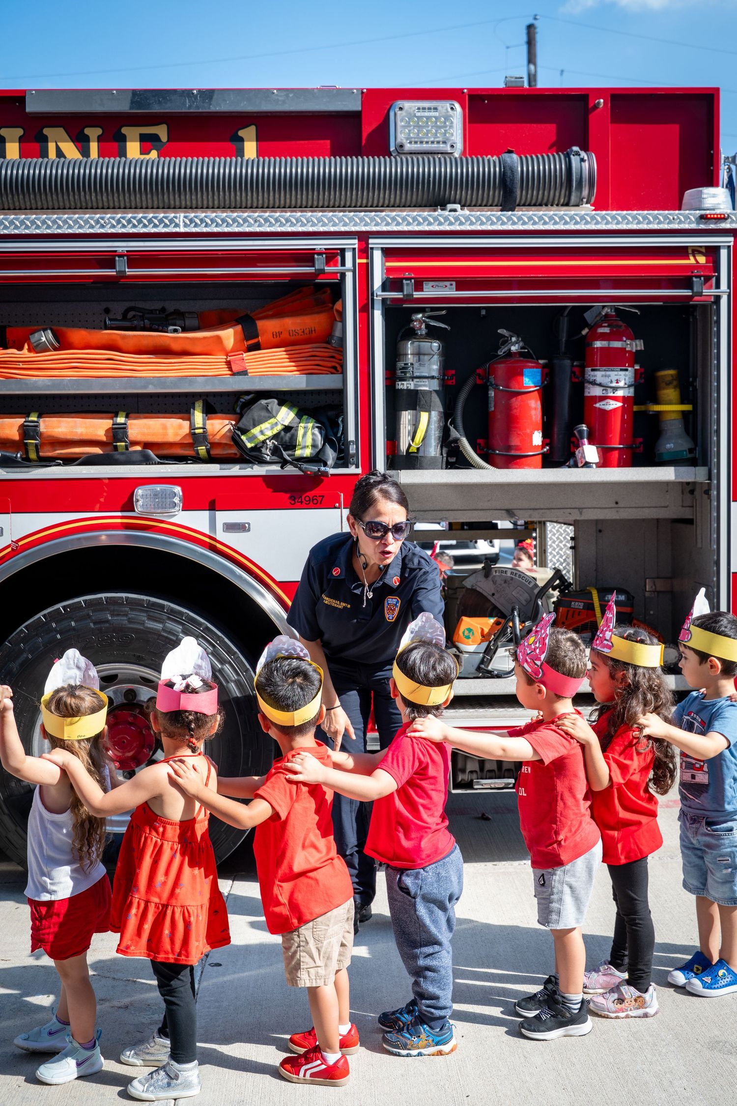 Firefighter showing children fire truck equipment during a school field trip safety education event outdoors.