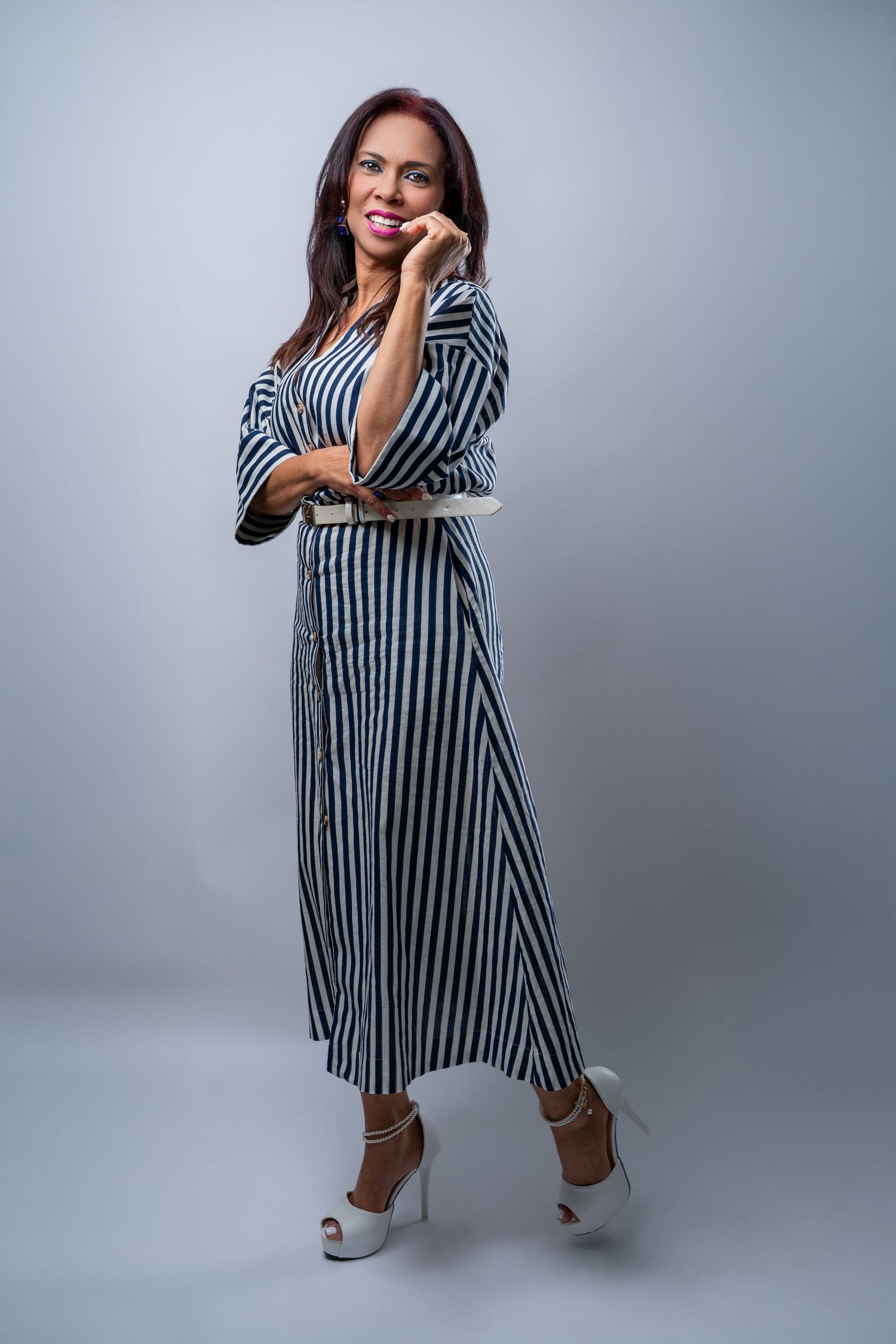 A stylish black and white striped maxi dress with high heels poses against a grey studio background.