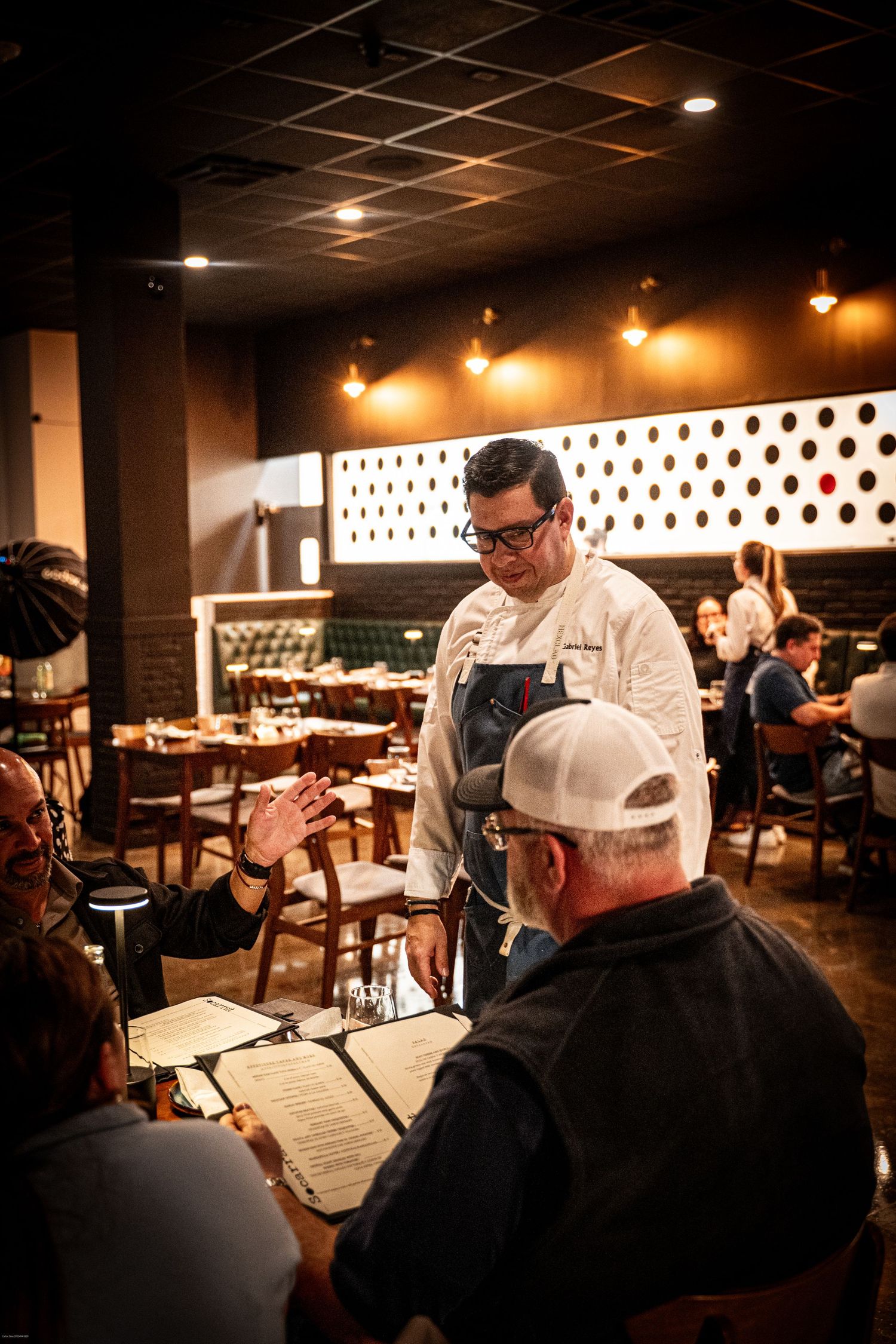 Diners seated at a dimly lit restaurant with warm ambient lighting and polka dot wall decor.