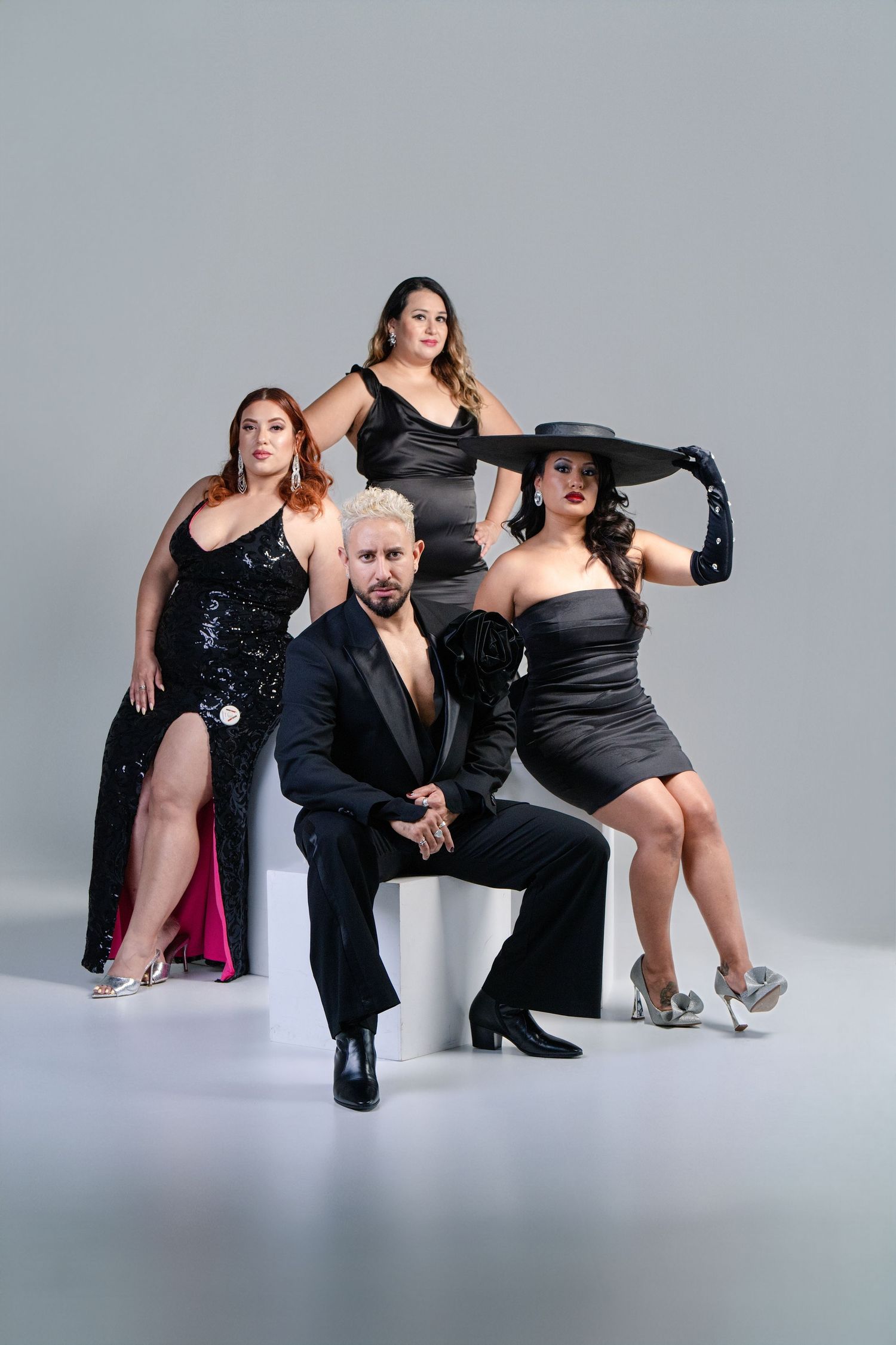 A group performs dramatic poses in black outfits against a light gray backdrop in a fashion photo series.