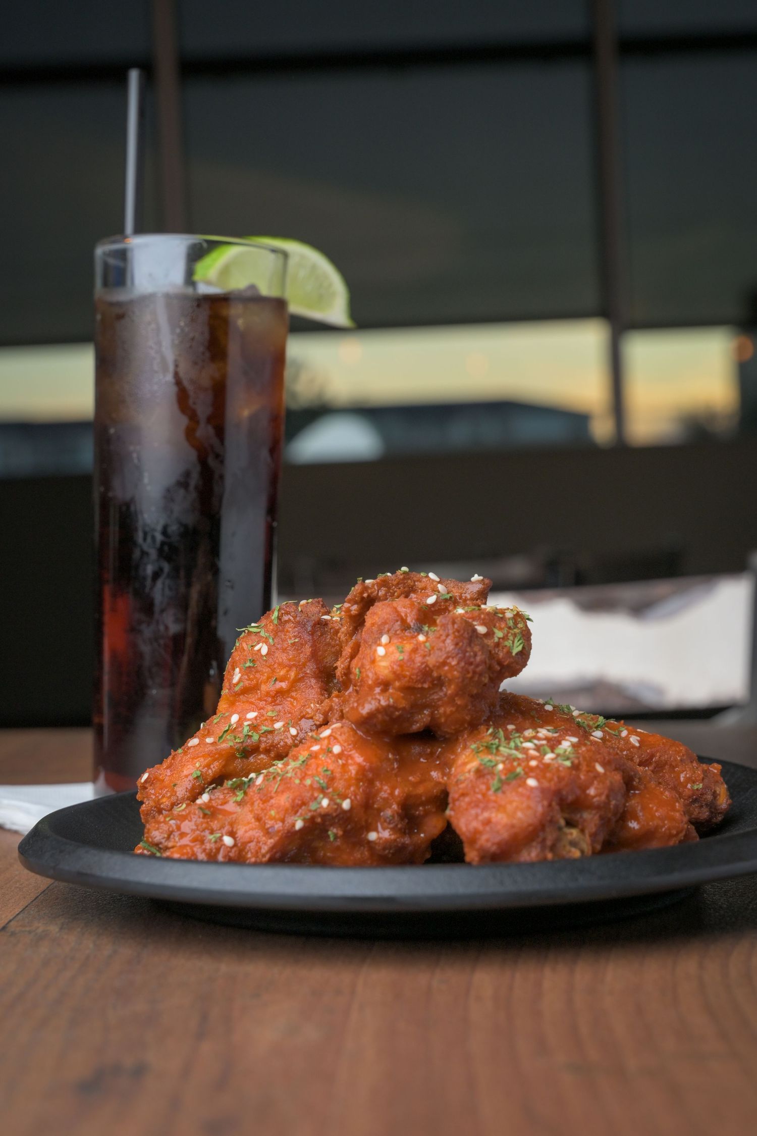 Spicy glazed chicken wings with sesame seeds served with cola on dark plate.