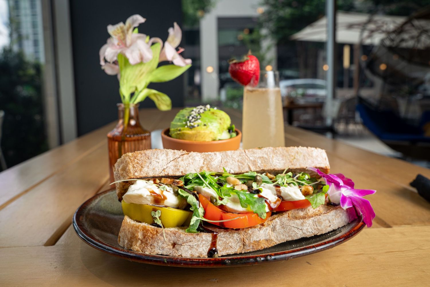 Artisanal sandwich plate with fresh vegetables and garnishes on rustic wooden table.