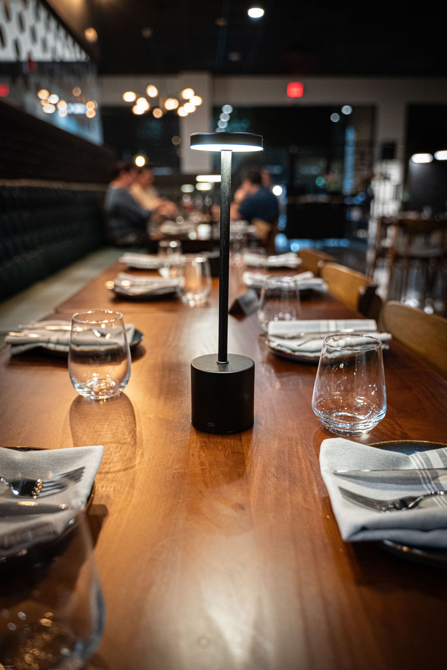 Place settings with wine glasses arranged on a long wooden dining table under moody lighting in an upscale restaurant.