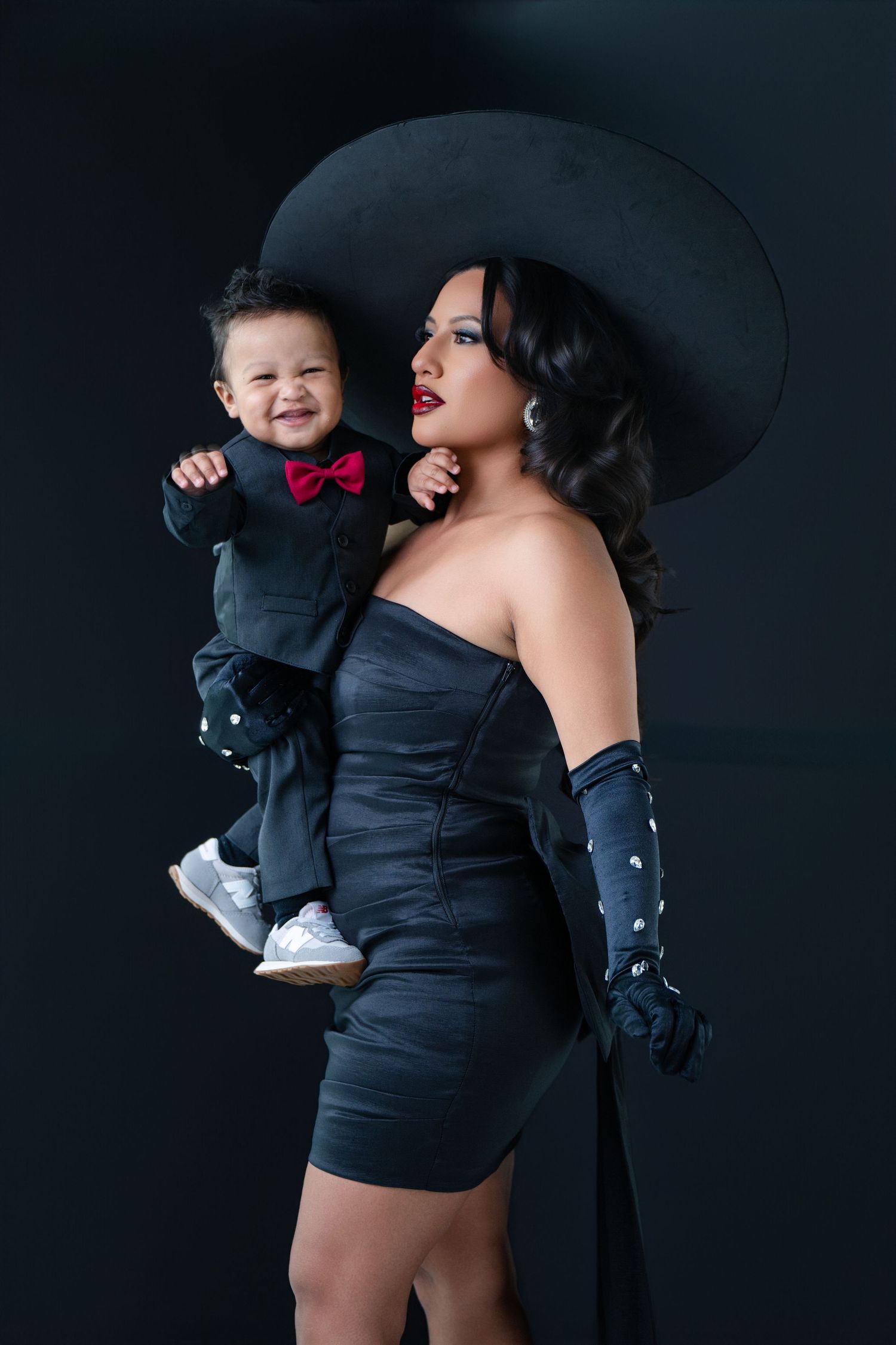 Elegant black and red formal wear portrait against dark background featuring a wide brimmed hat and matching attire.