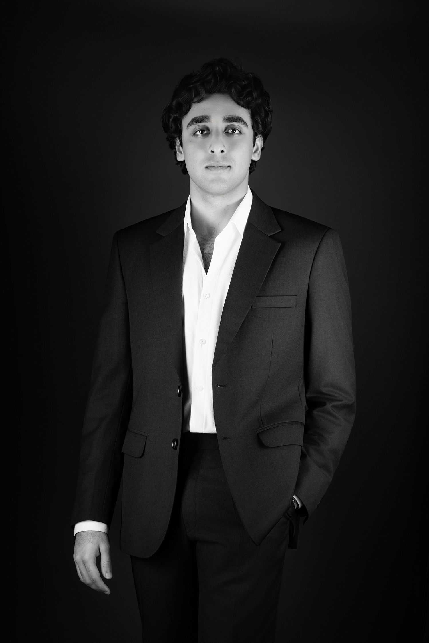 Professional black and white portrait series showing person in classic black suit and white shirt against dark background.