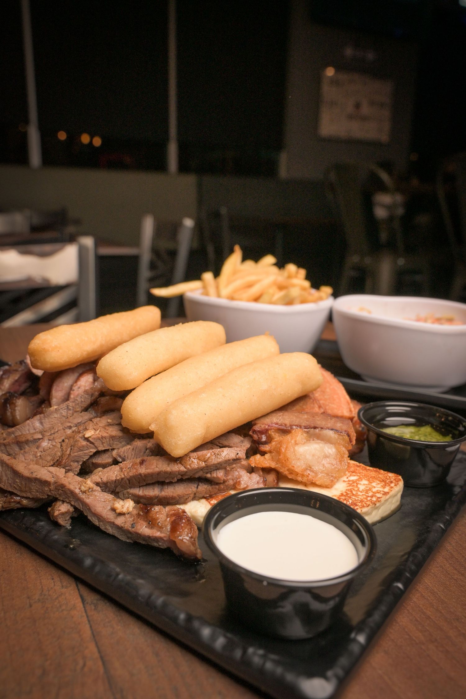 Platter with breadsticks, dipping sauce and meat served on a dark slate board.