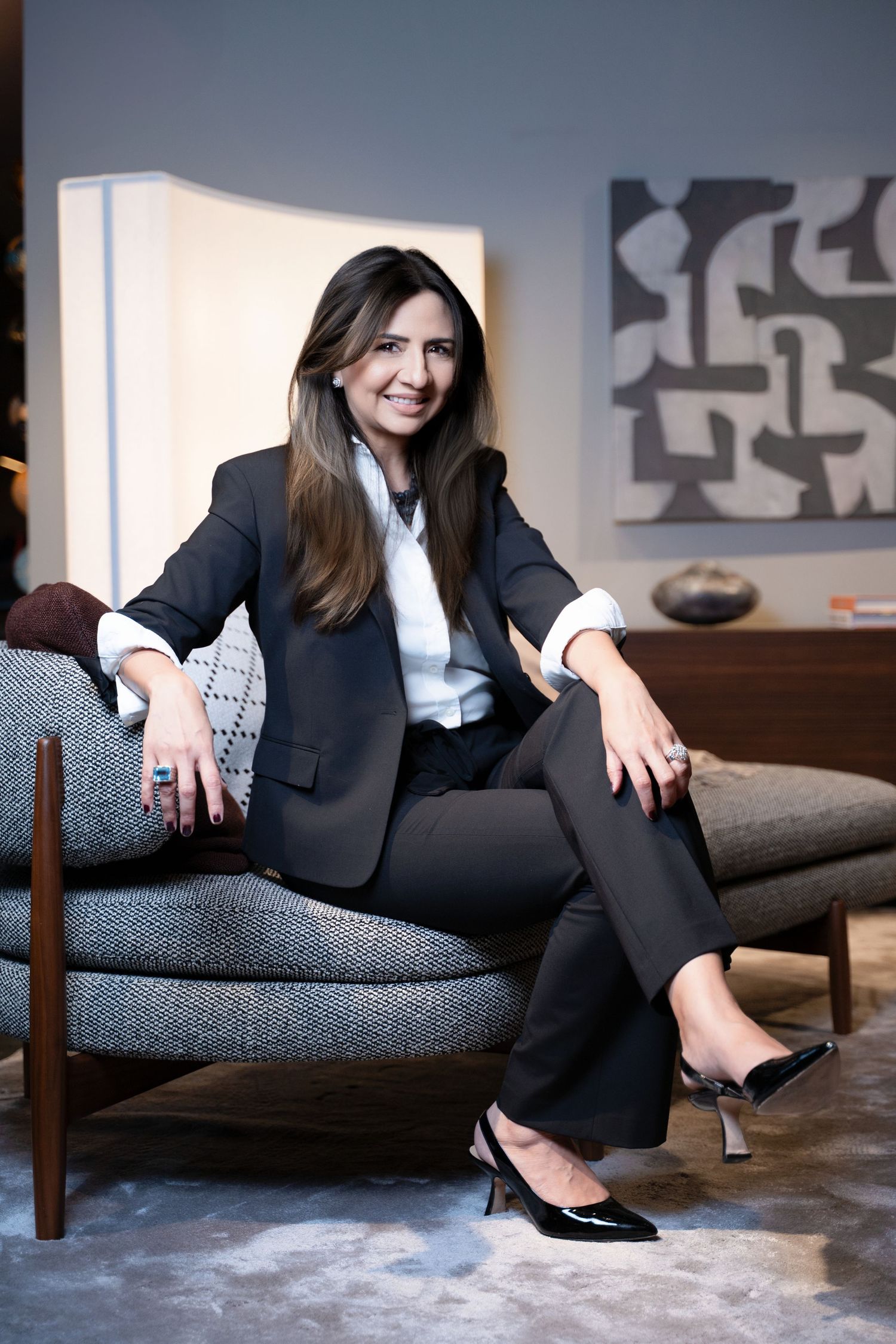 Business portrait of person in dark suit relaxing on gray sofa with modern art in background.